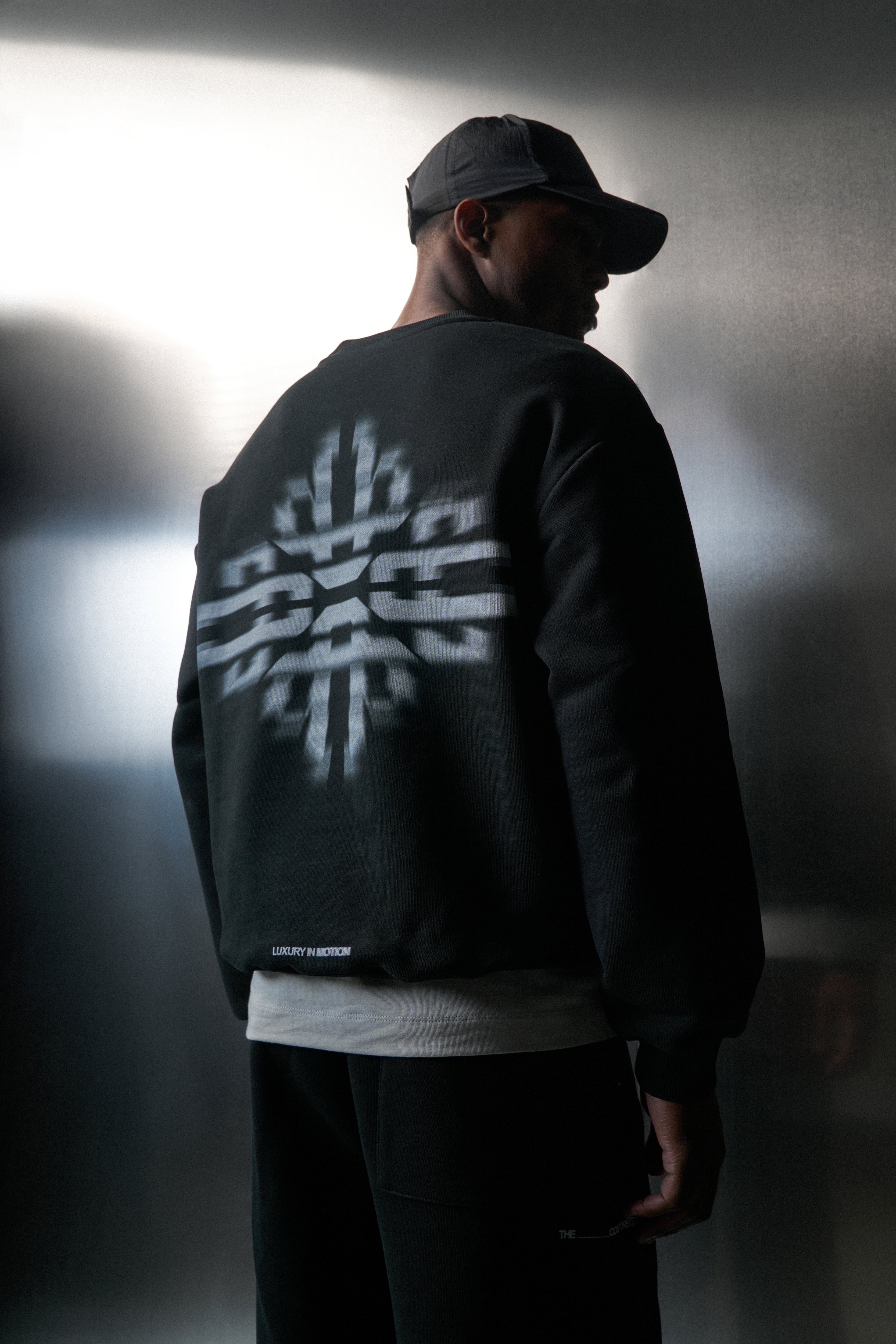 Person wearing a black sweatshirt with a white logo on the back against a grey background