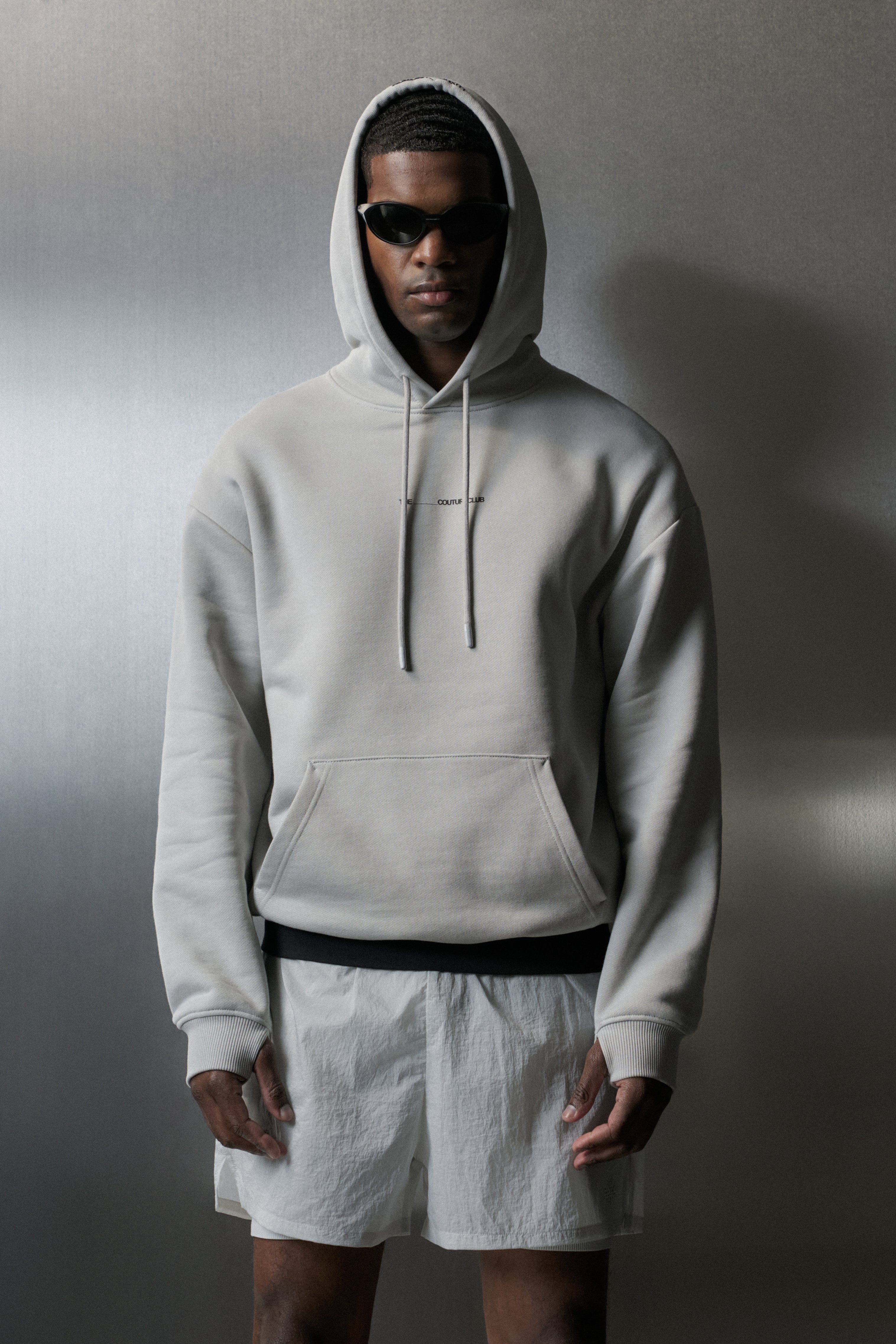 Person wearing a light grey hoodie and white shorts against a neutral background