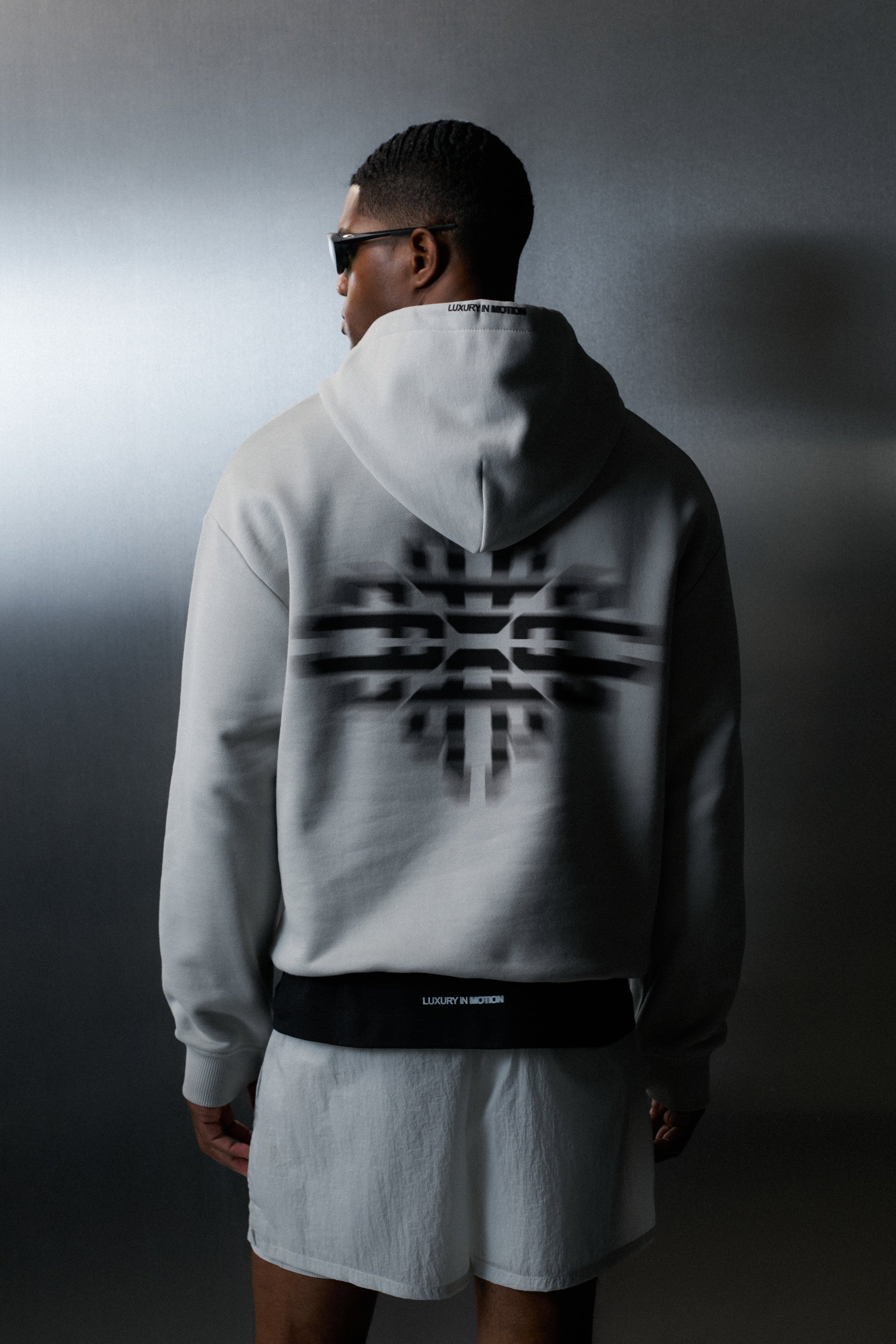 Person wearing a grey hoodie with a black logo on the back against a dark background