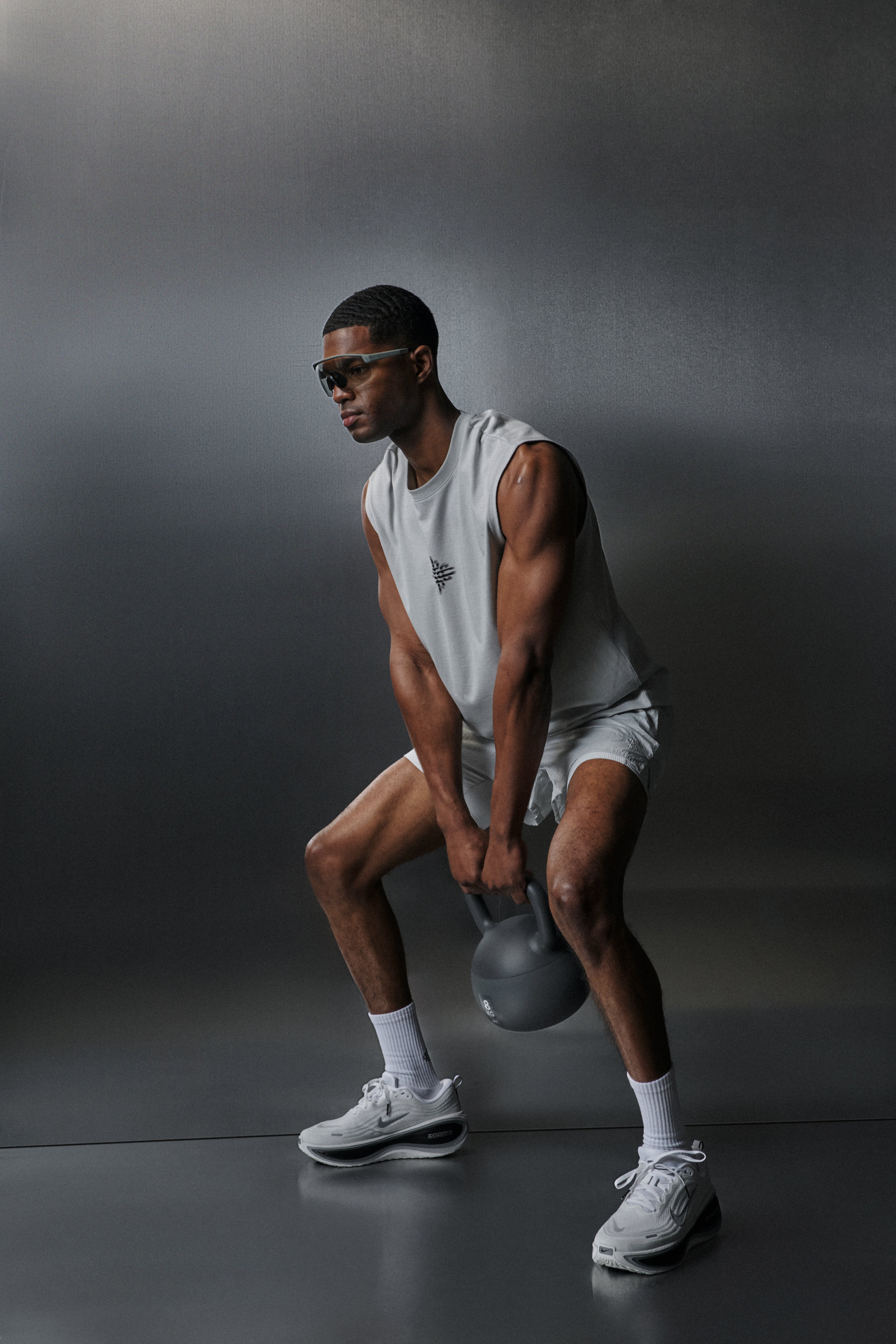 Man lifting a kettlebell in a white vest against a dark background