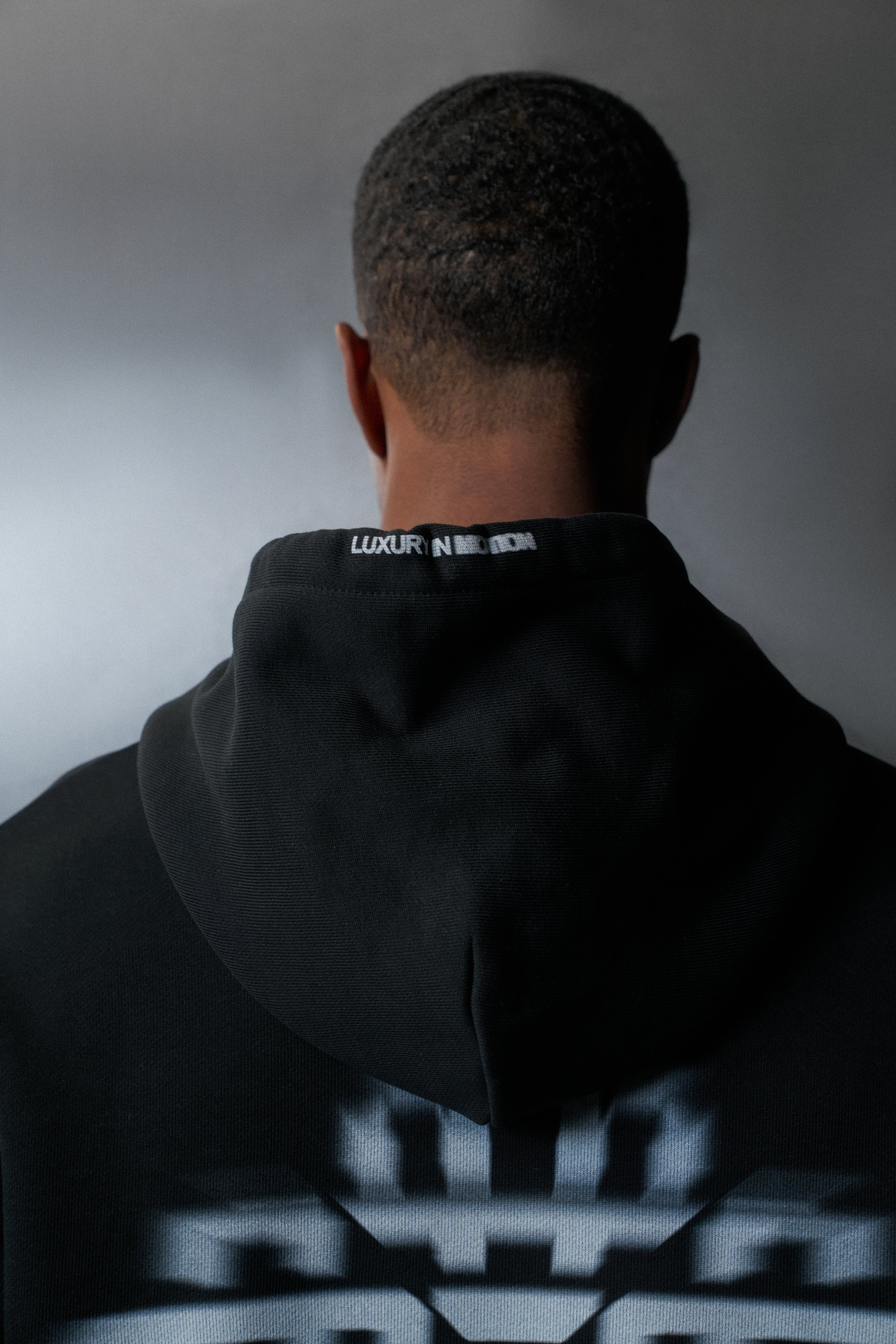Person wearing a black hoodie with visible branding on a grey background