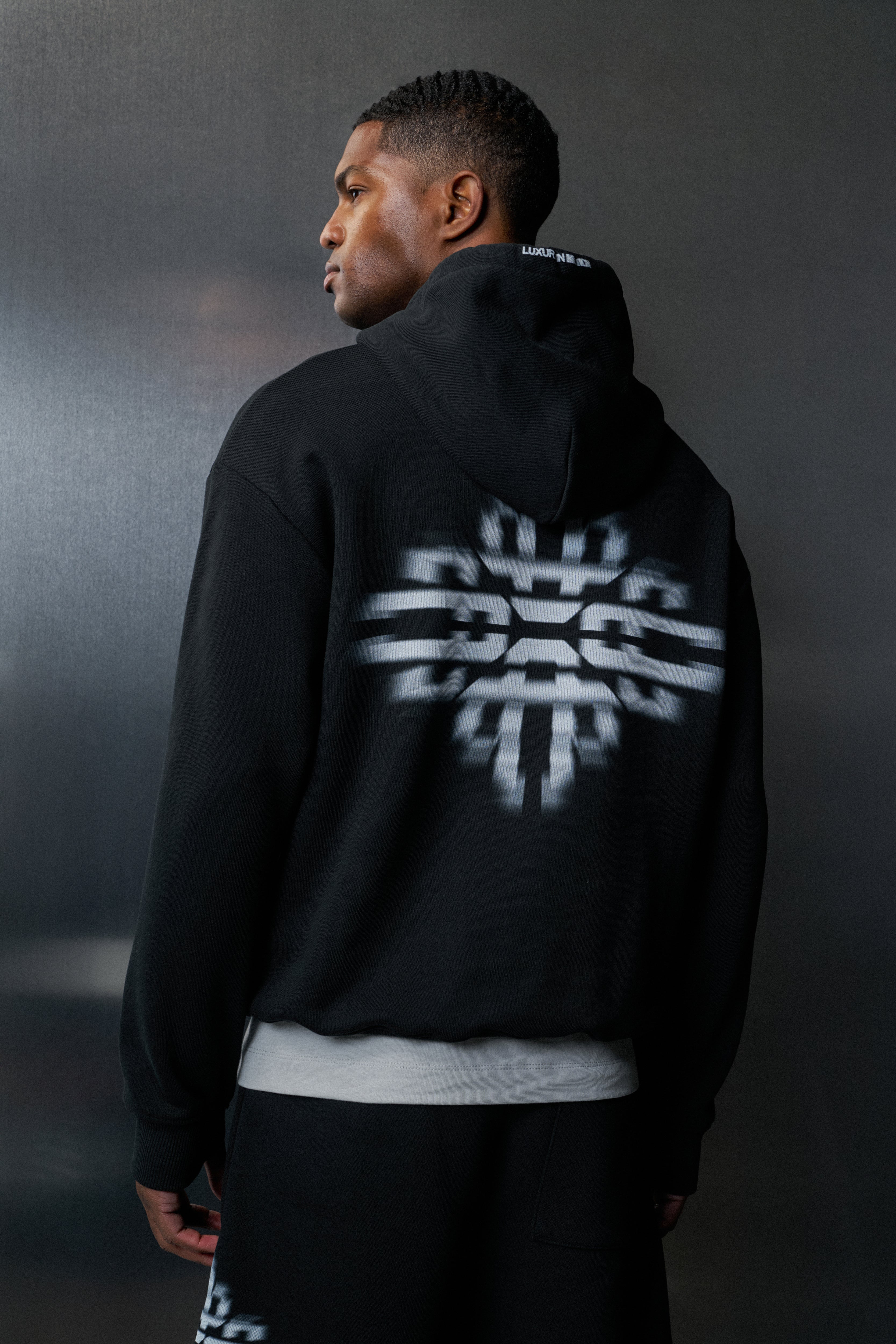 Person wearing a black hoodie with a white logo on the back against a dark background