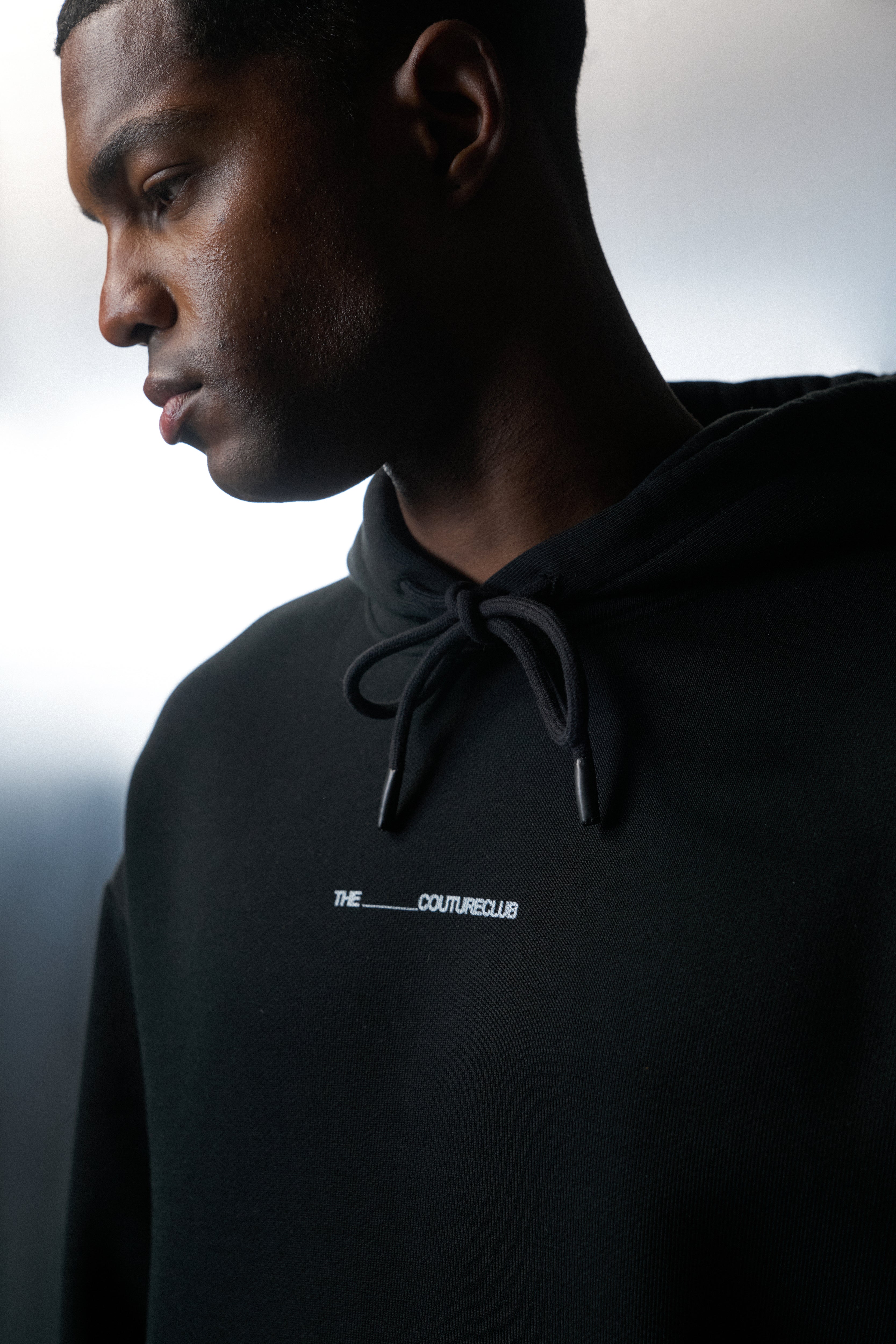 Person wearing a black hoodie with a logo on a blurred background