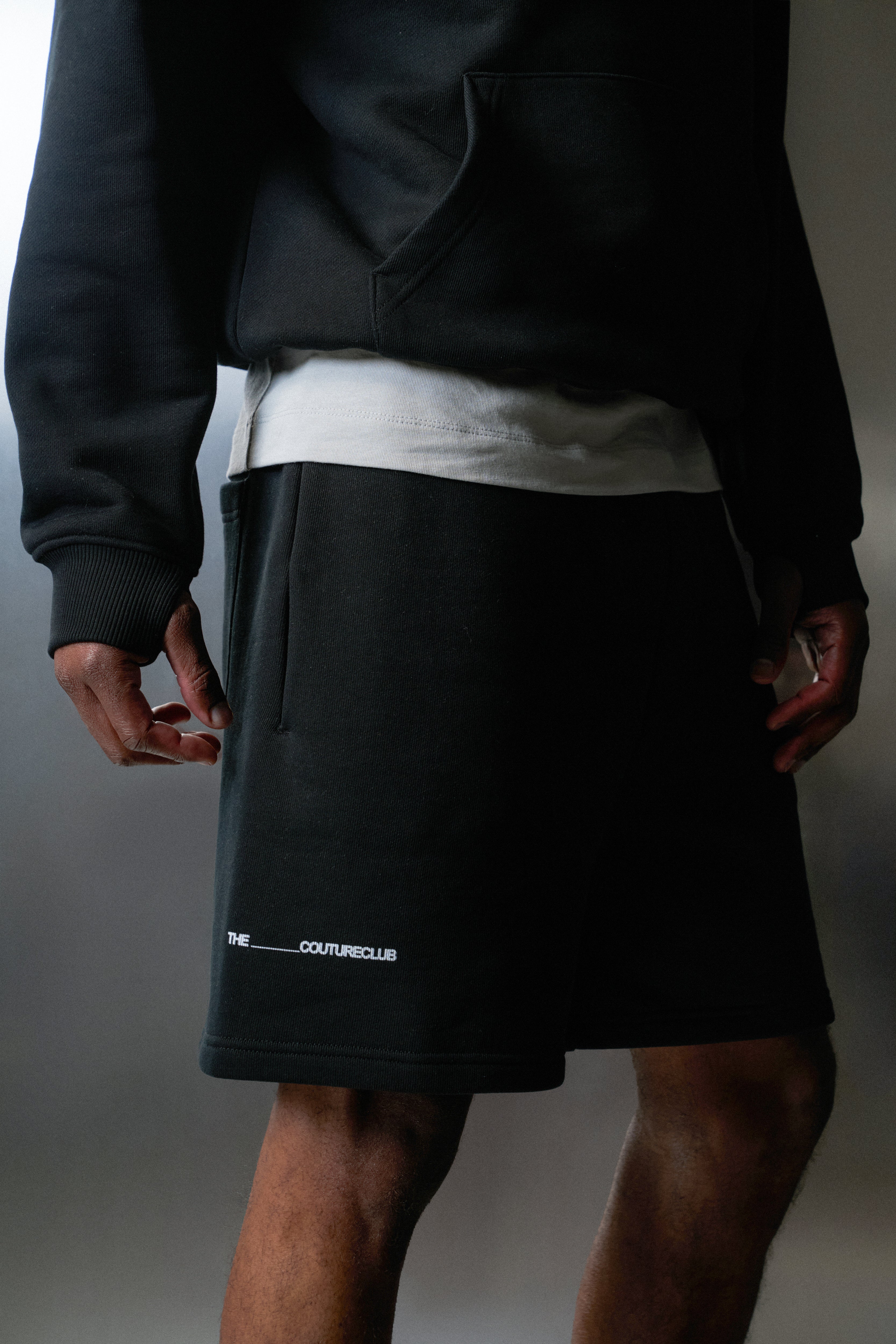 Person wearing a black outfit with a visible brand logo on a grey background