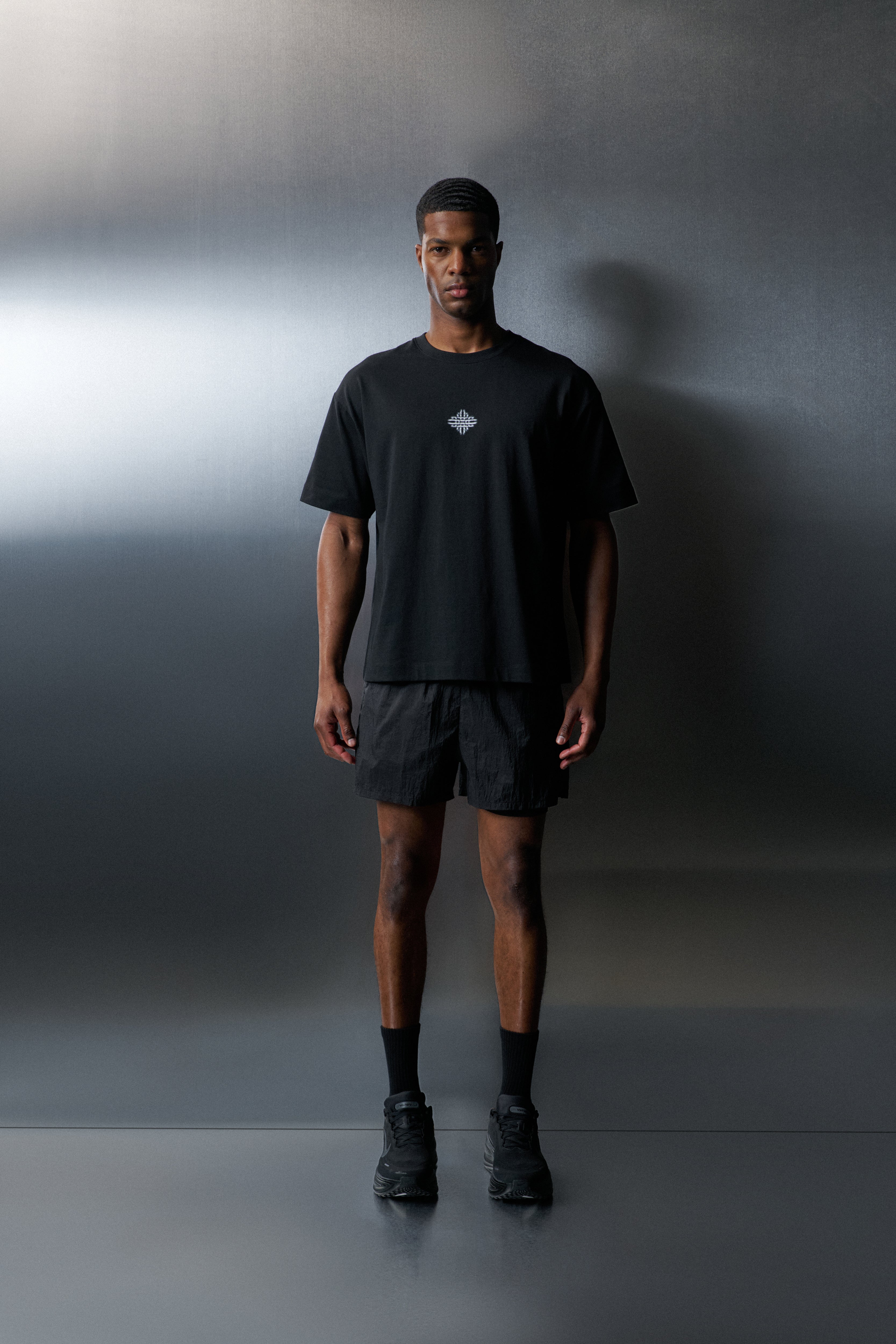 Person wearing a black t-shirt, shorts, and shoes against a gradient gray background