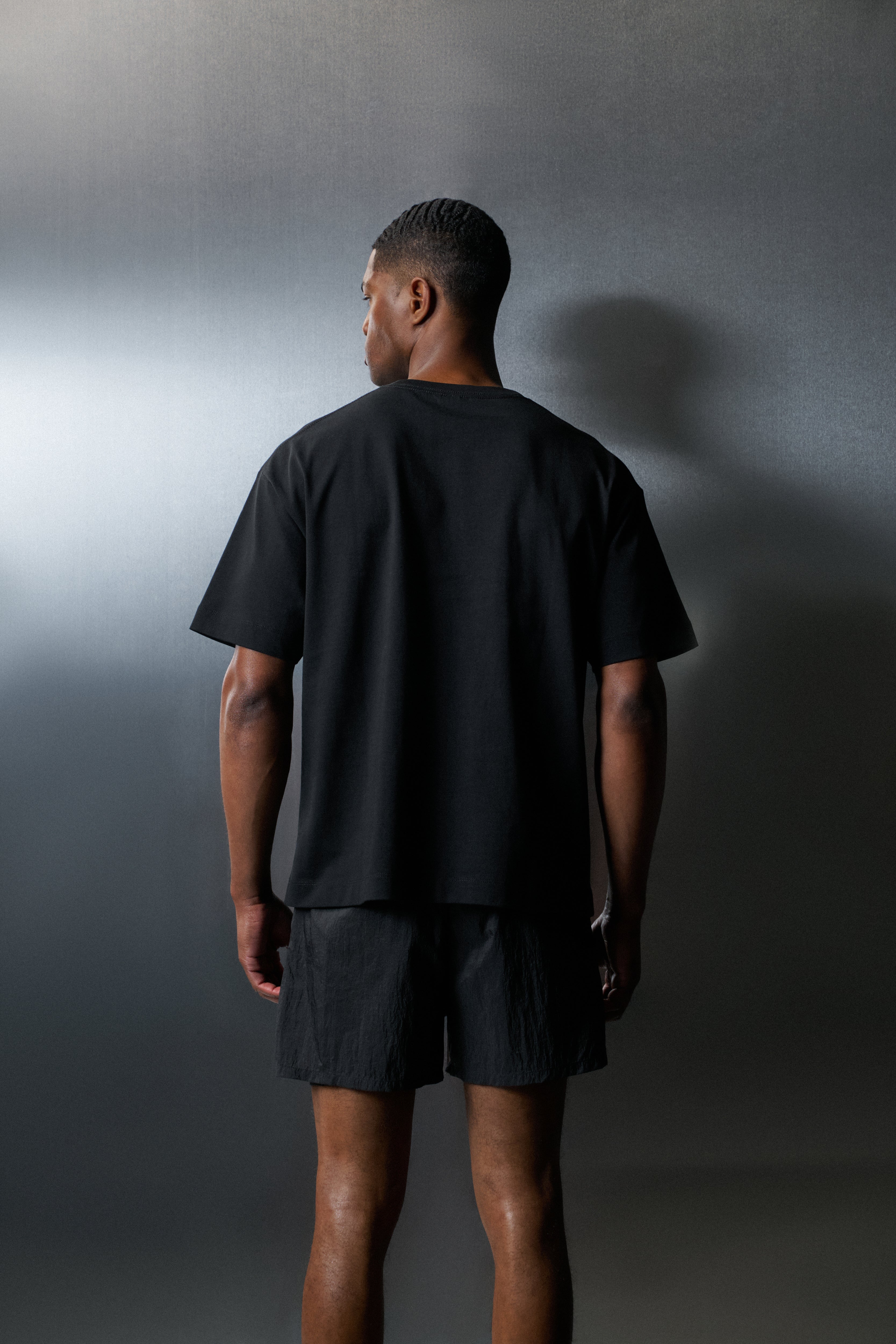 Person wearing a black t-shirt and shorts standing against a grey background