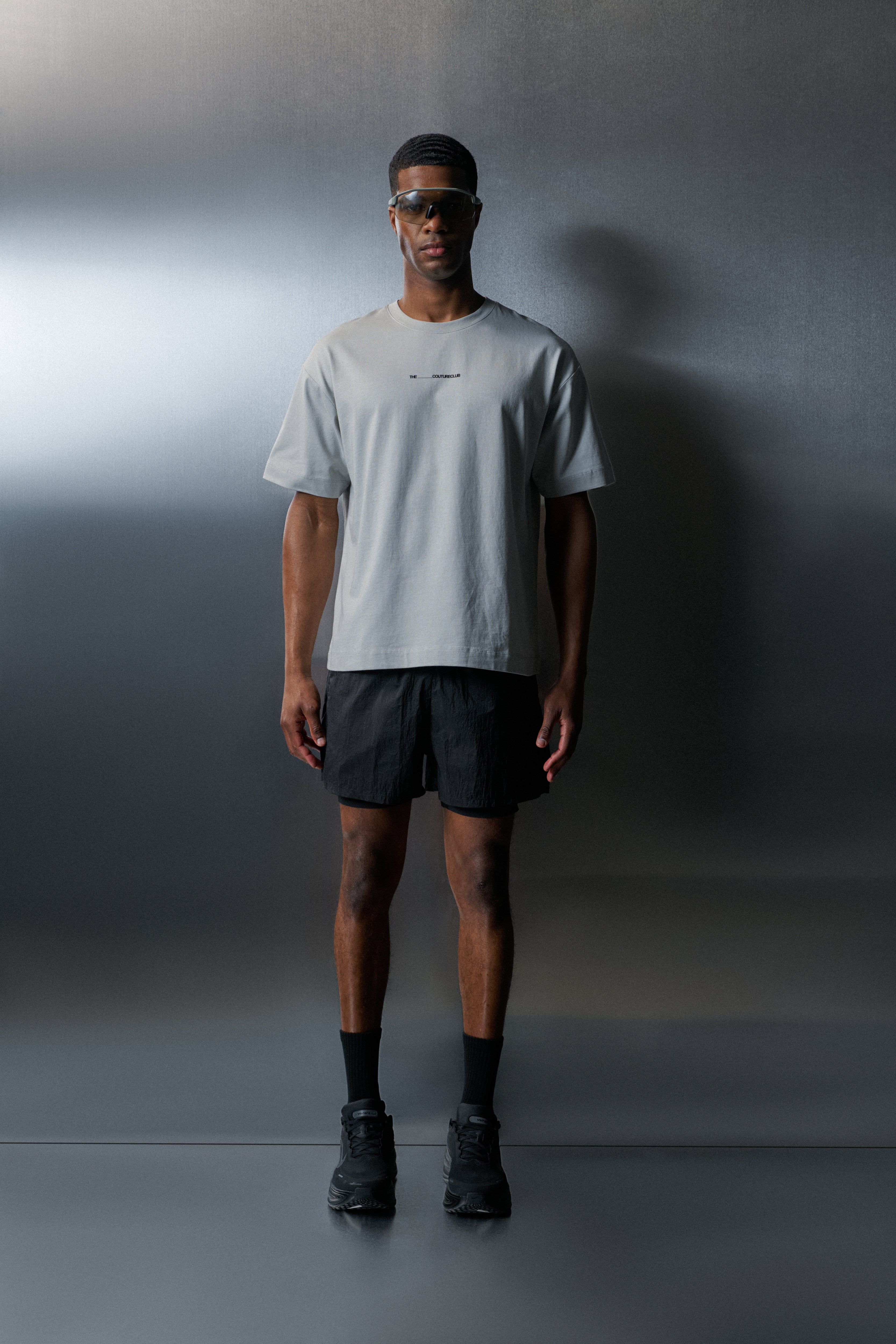 Person wearing a light grey t-shirt and black shorts against a dark background