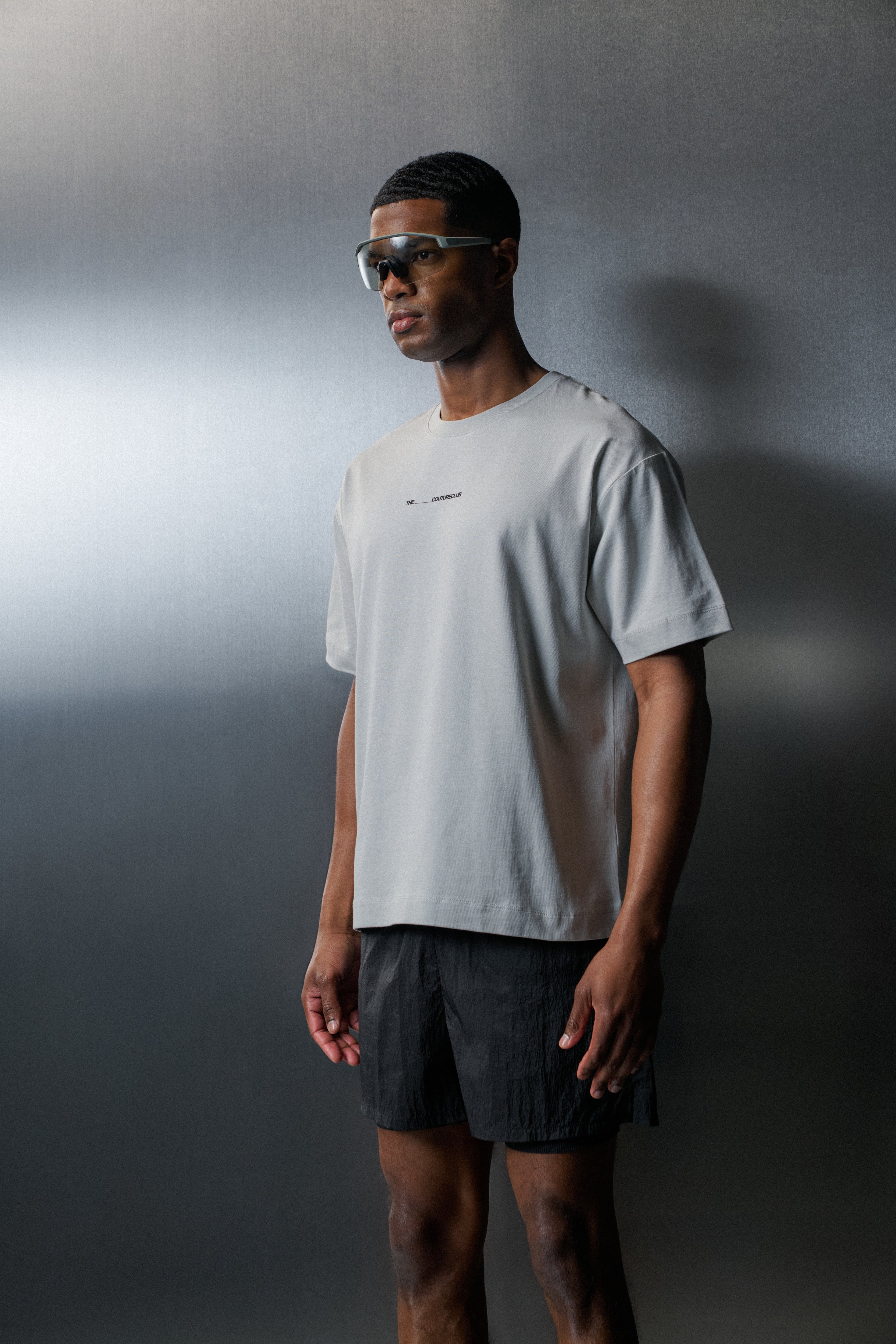 Man wearing a white t-shirt and dark shorts against a grey background