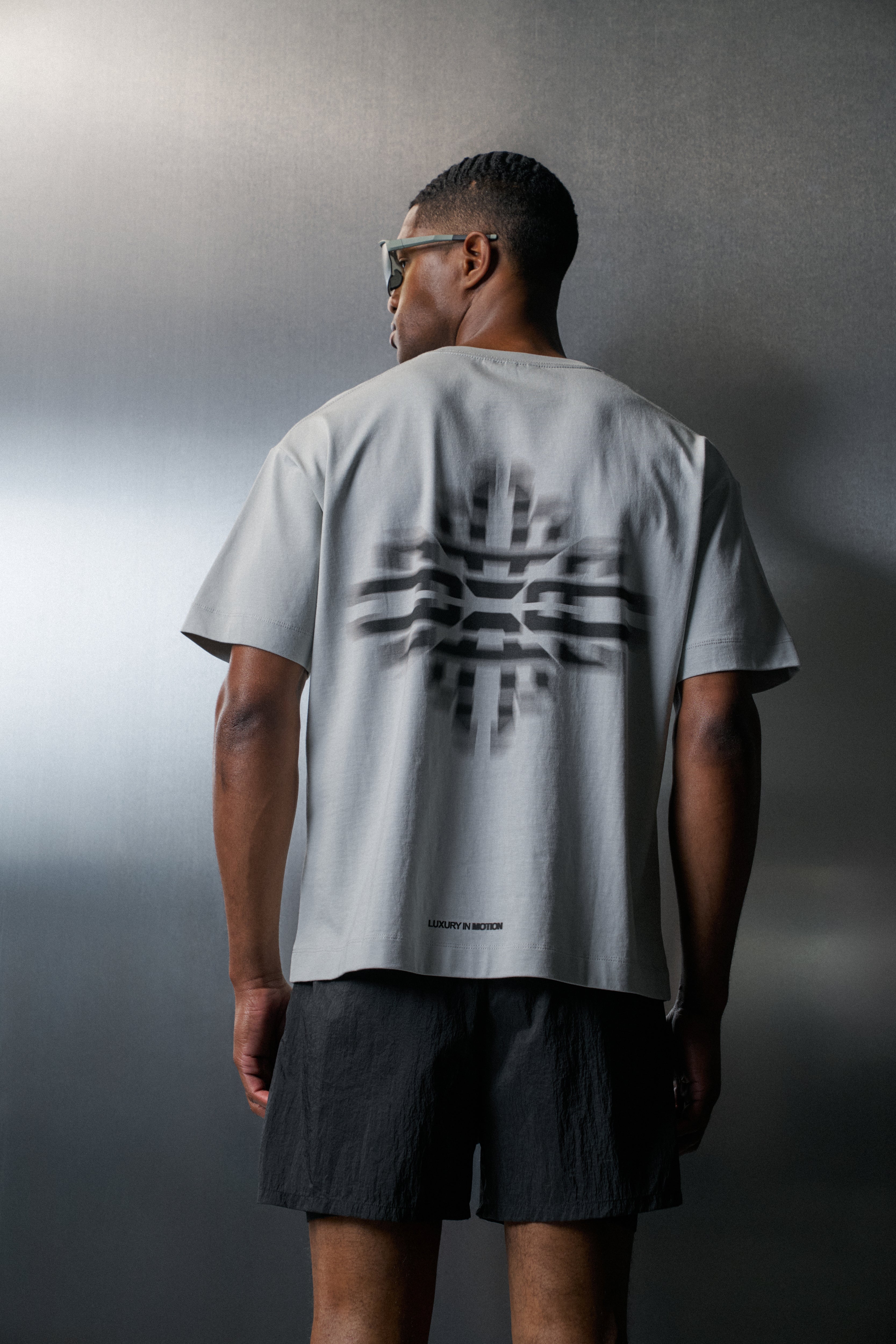 Person wearing a light grey t-shirt with a black graphic design on the back, standing against a grey background.