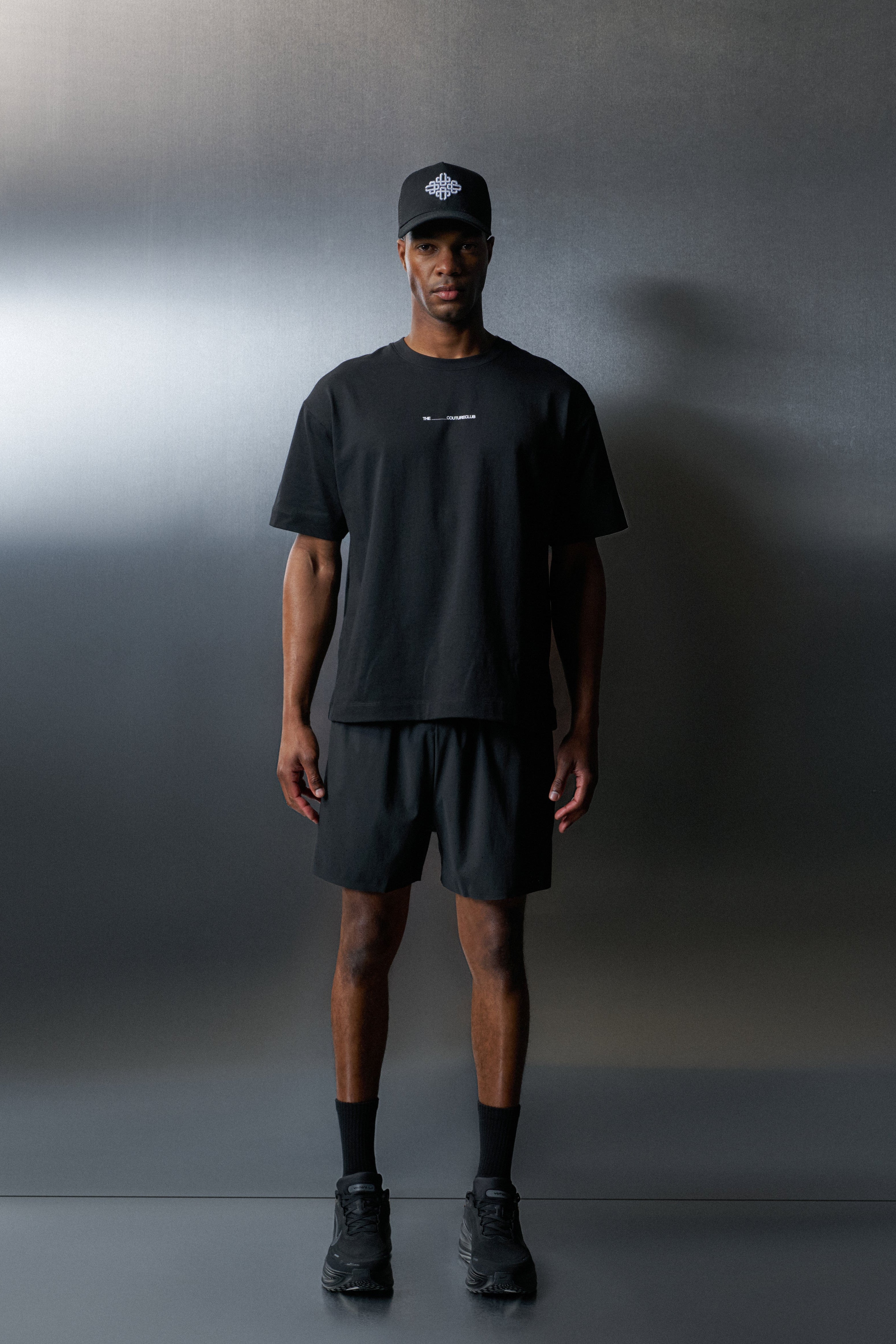 Person wearing a black t-shirt, shorts, and cap against a grey background