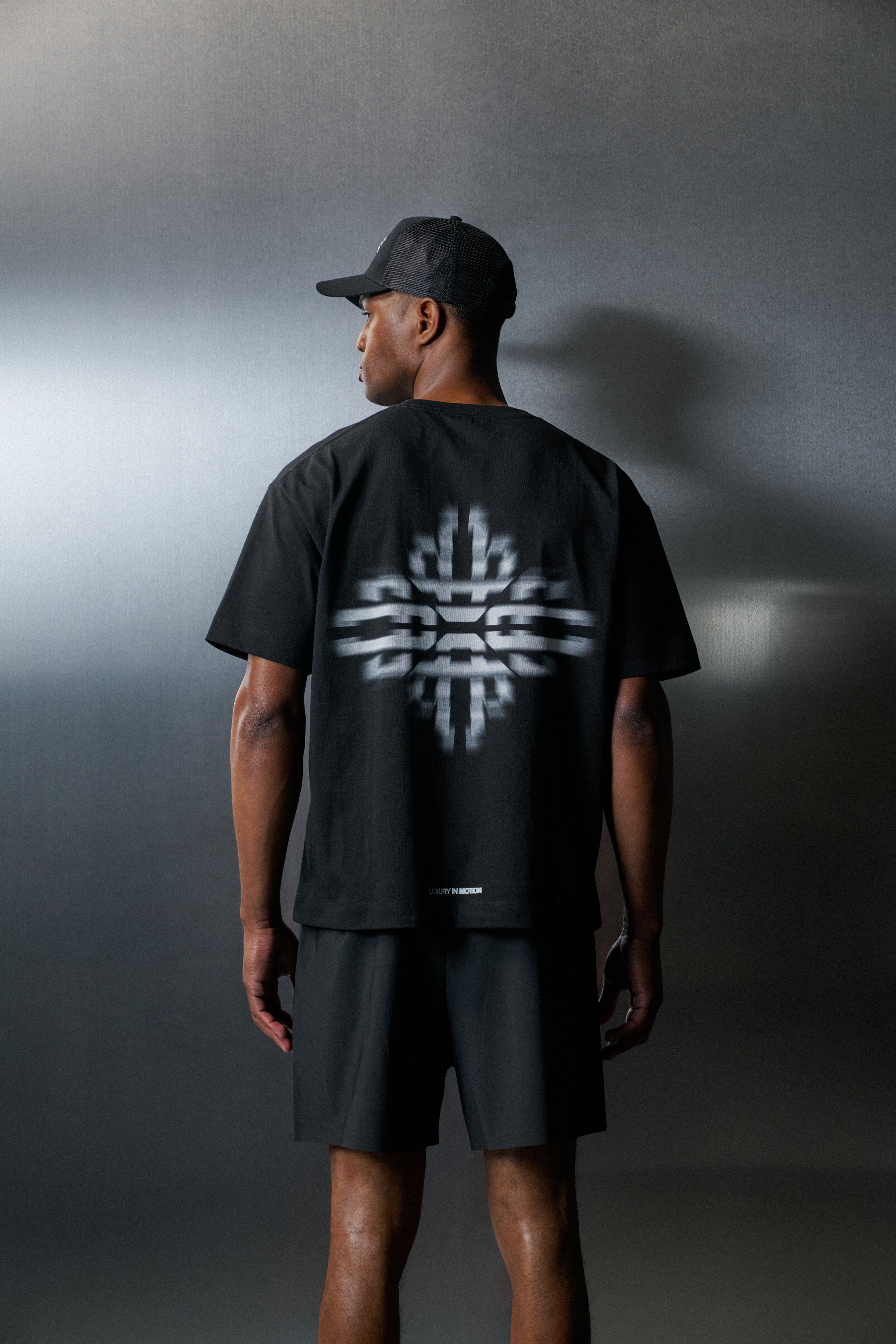 Person wearing a black t-shirt with a white logo on the back against a grey background