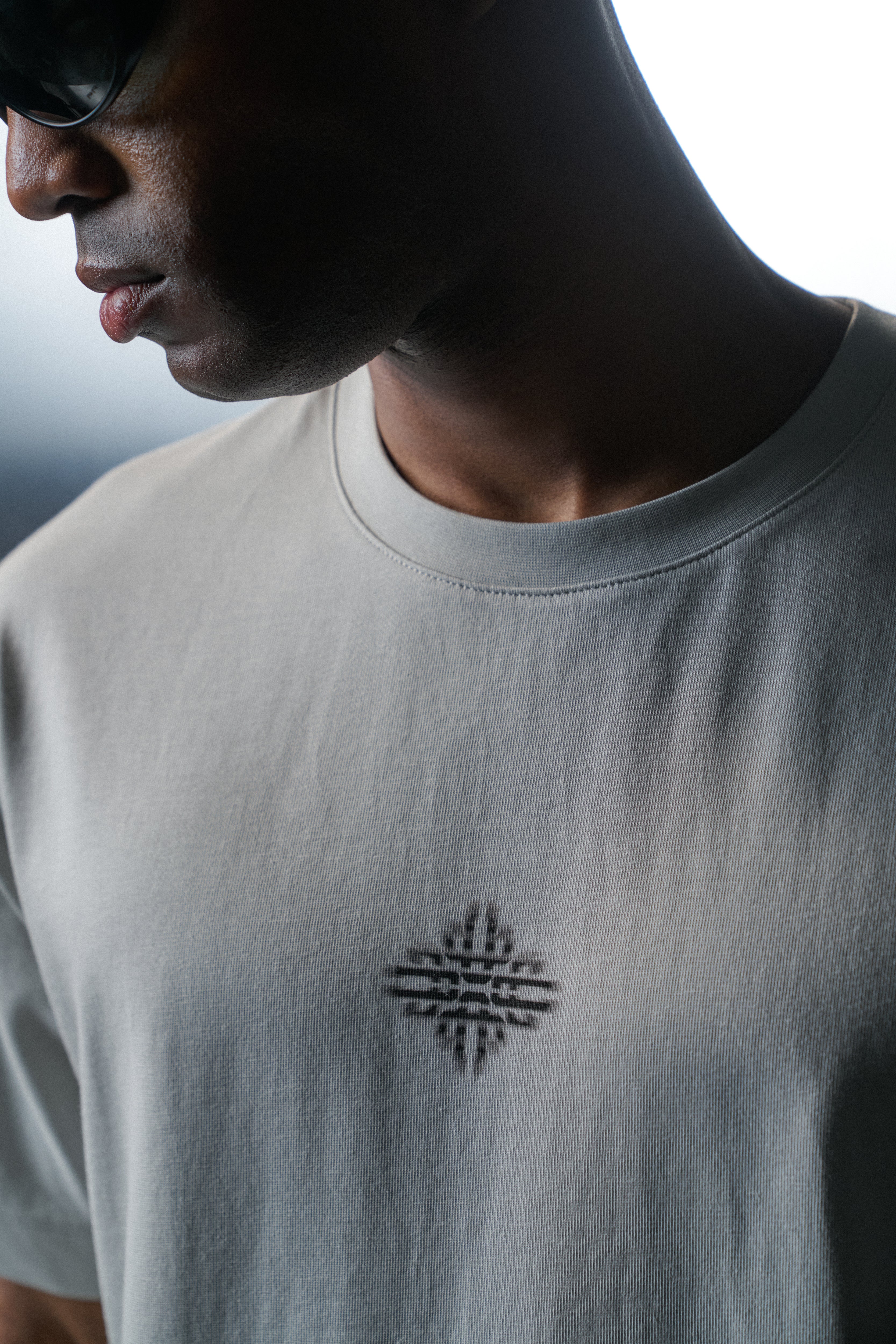 Person wearing a light grey t-shirt with a black geometric design on a dark background