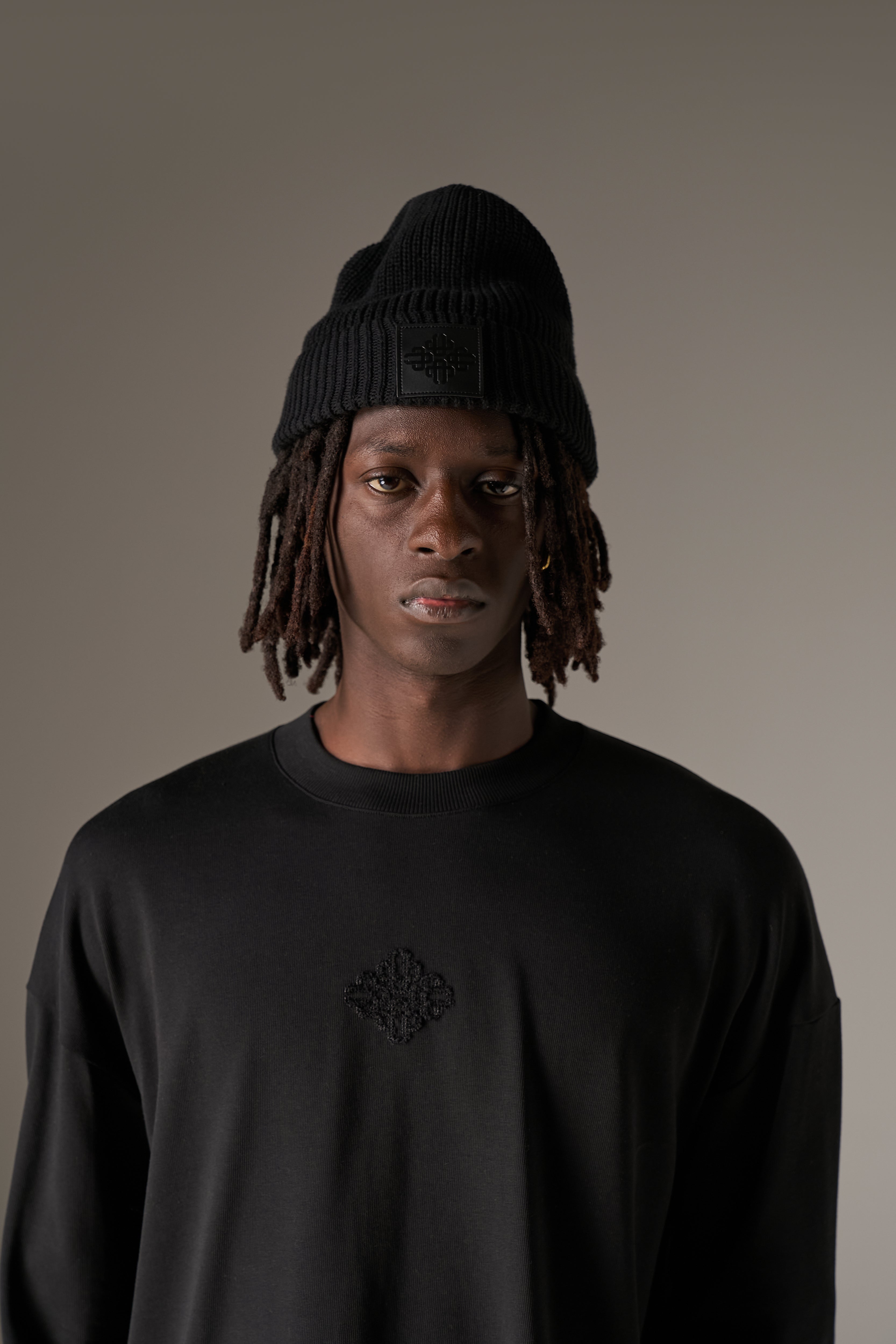 Man in a long sleeved black t-shirt and a beanie against a neutral background