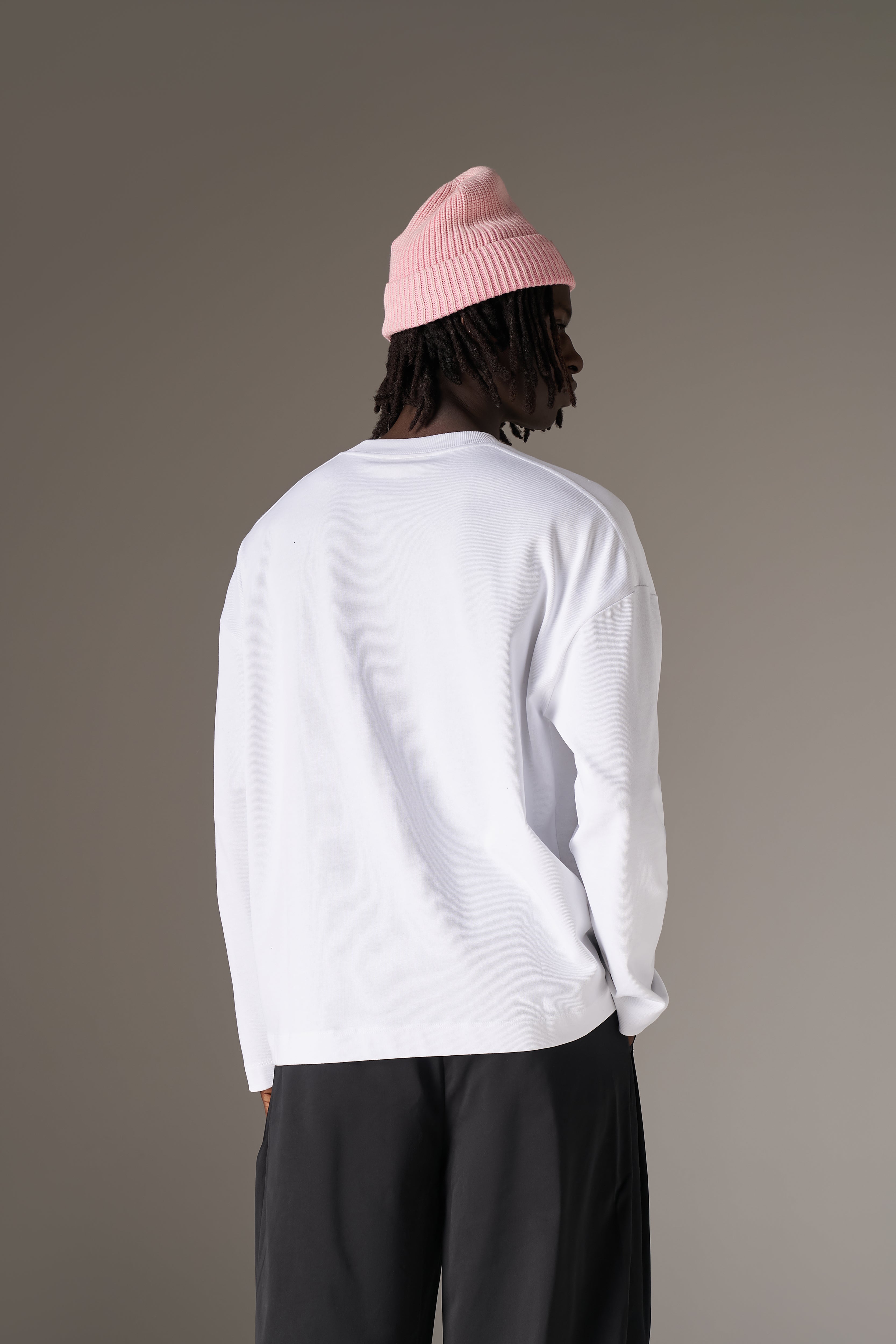 Person wearing a white long-sleeve t-shirt and black pants with a pink beanie on a grey background