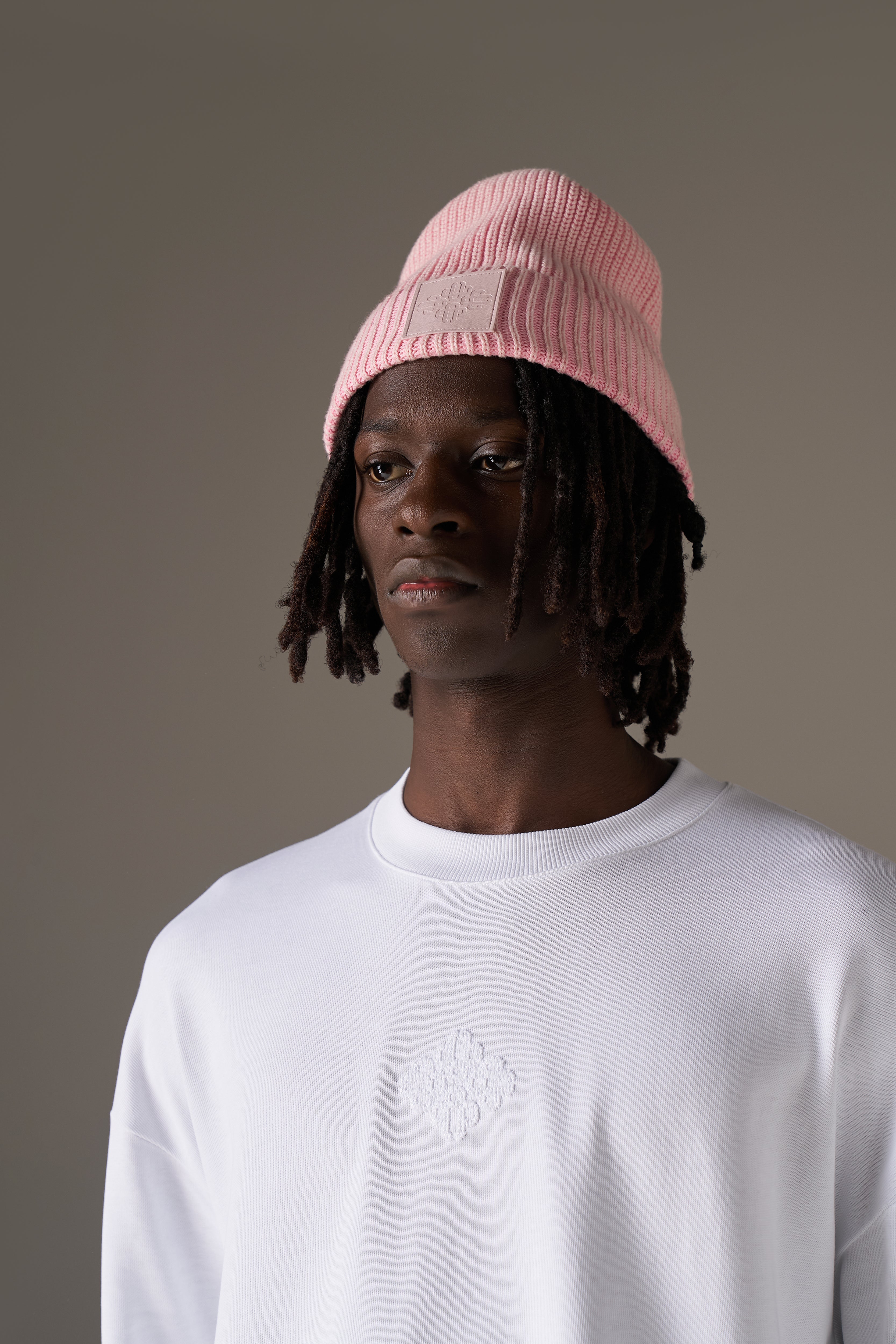 Person wearing a pink beanie and white long sleeve t-shirt against a grey background