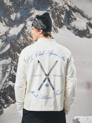 Person wearing a white long sleeved t-shirt with text and ski club logo against a snowy mountain background
