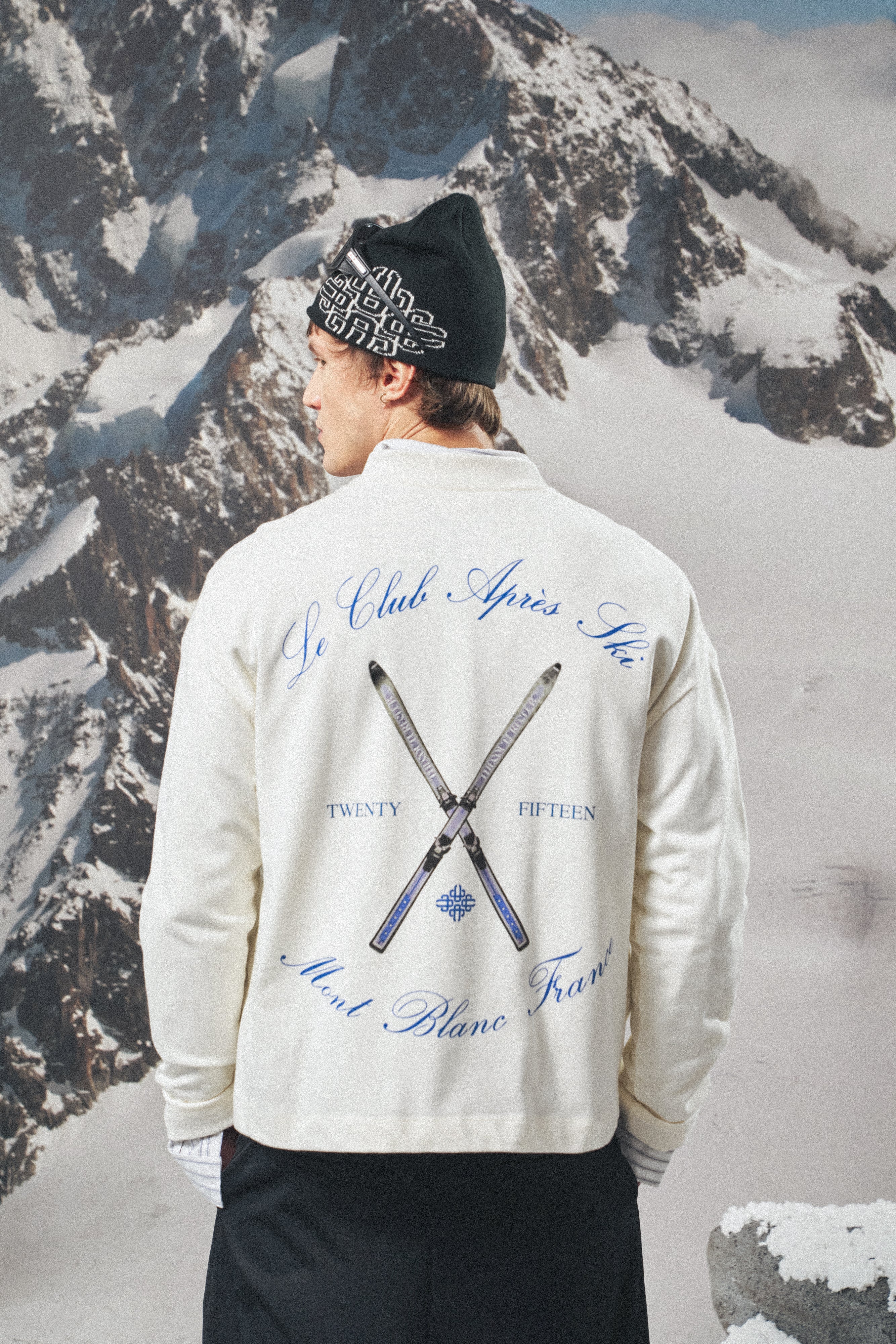 Person wearing a white long sleeved t-shirt with text and ski club logo against a snowy mountain background