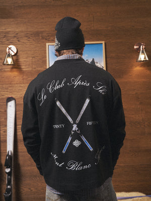 Person wearing a black long sleeved t-shirt with white text and graphics, standing in a room with wooden walls and a framed picture.