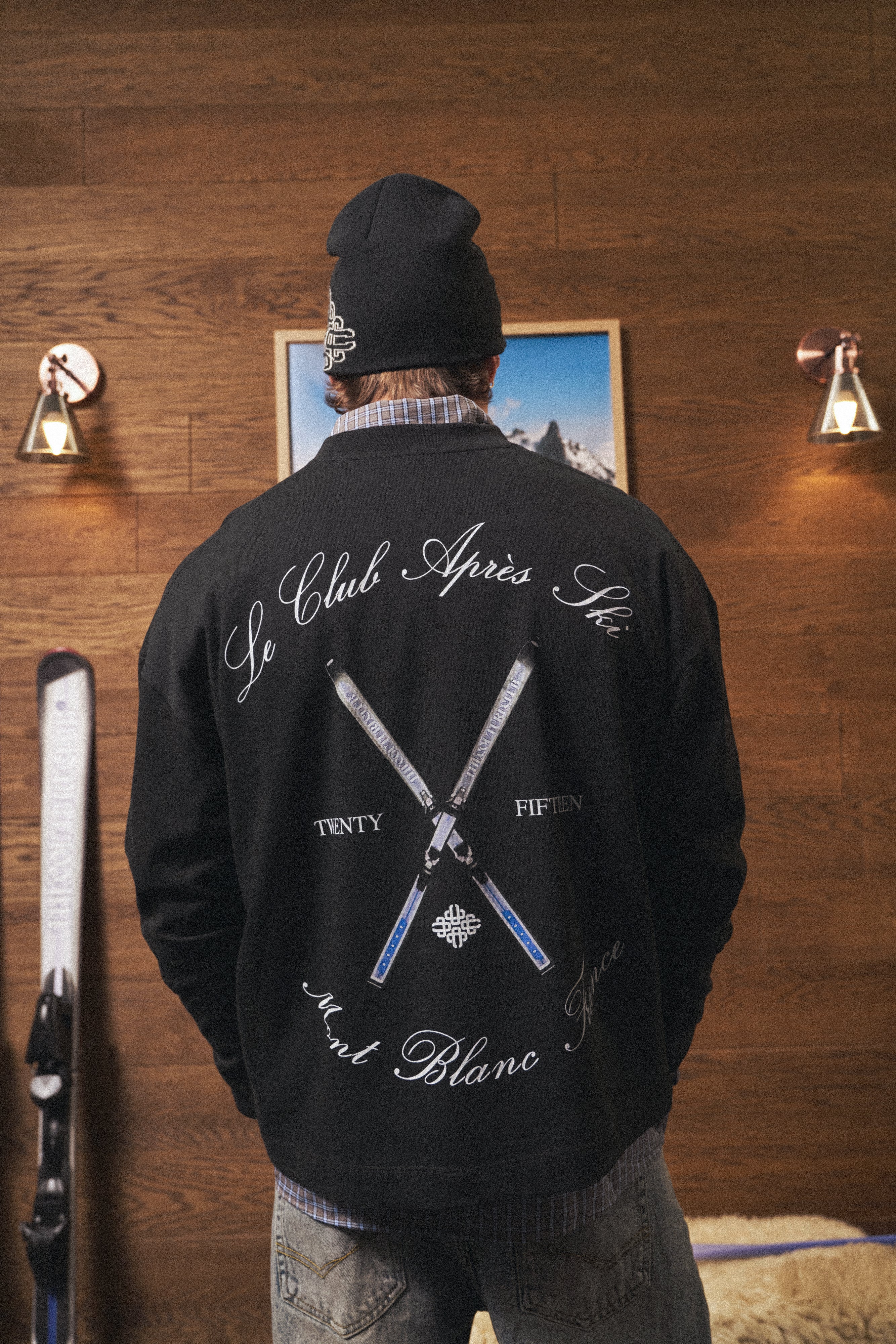 Person wearing a black long sleeved t-shirt with white text and graphics, standing in a room with wooden walls and a framed picture.