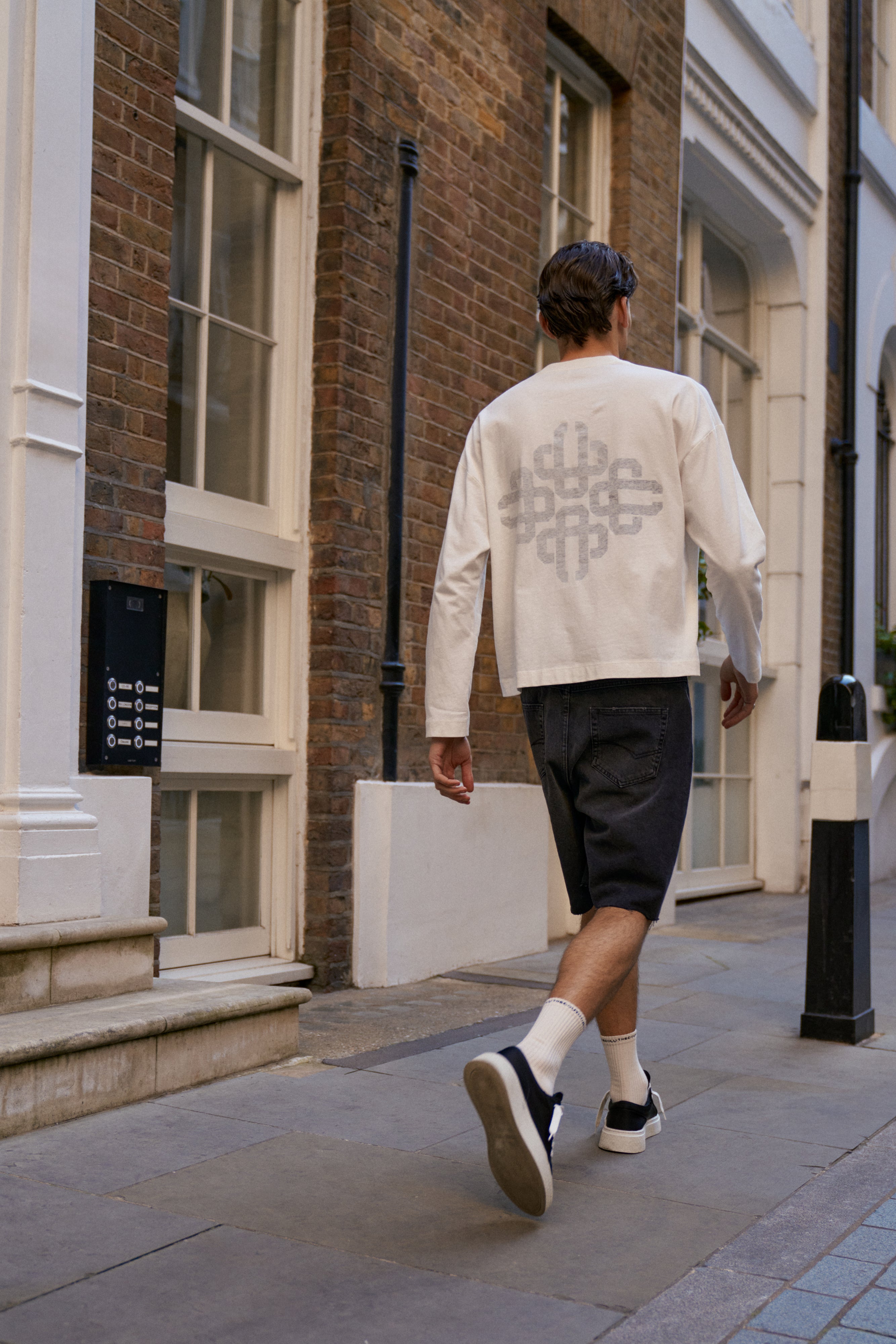 Person walking down a street wearing a white t-shirt with a geometric design.