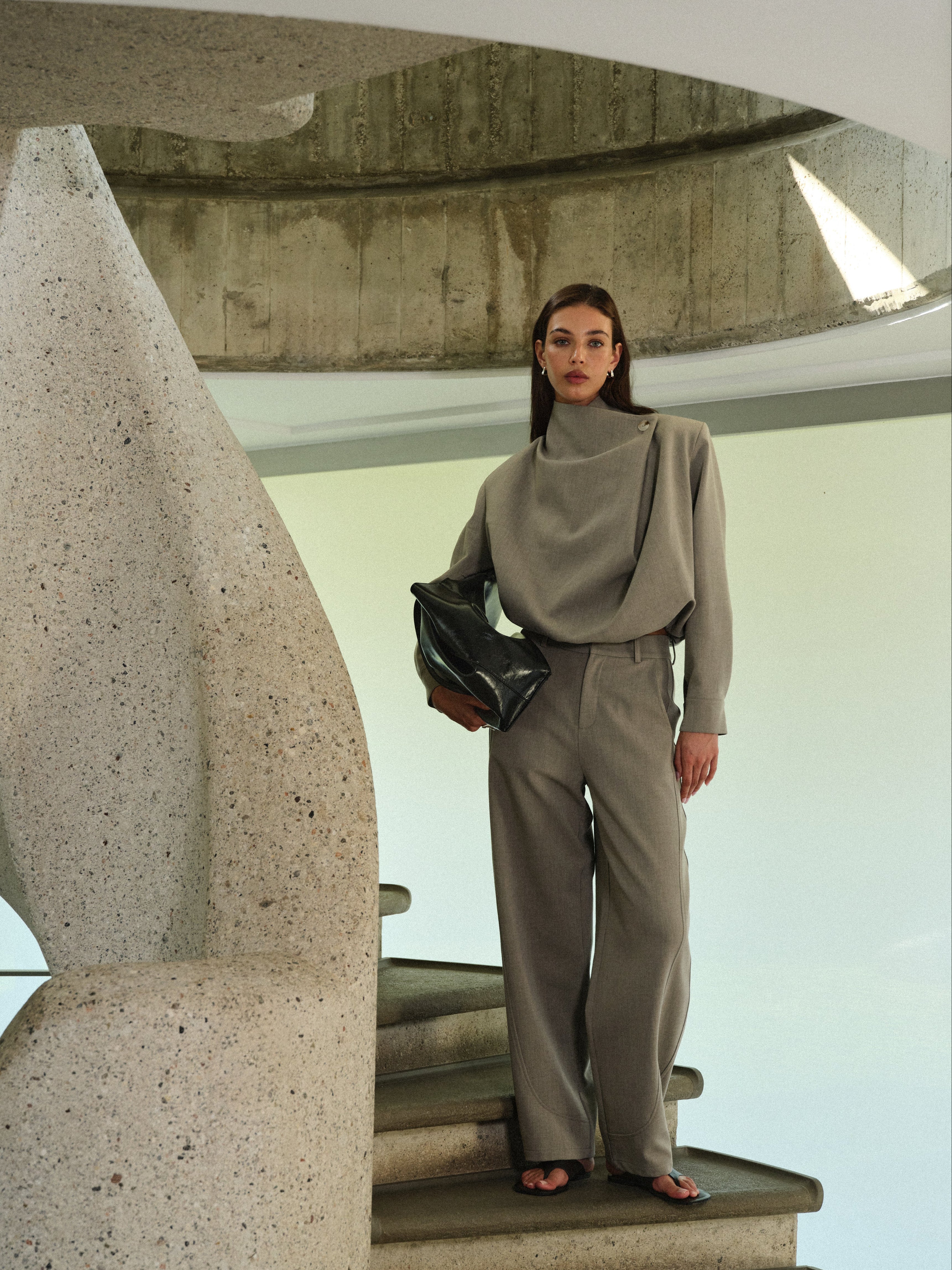 Woman in a grey matching tailored set standing on a spiral staircase.