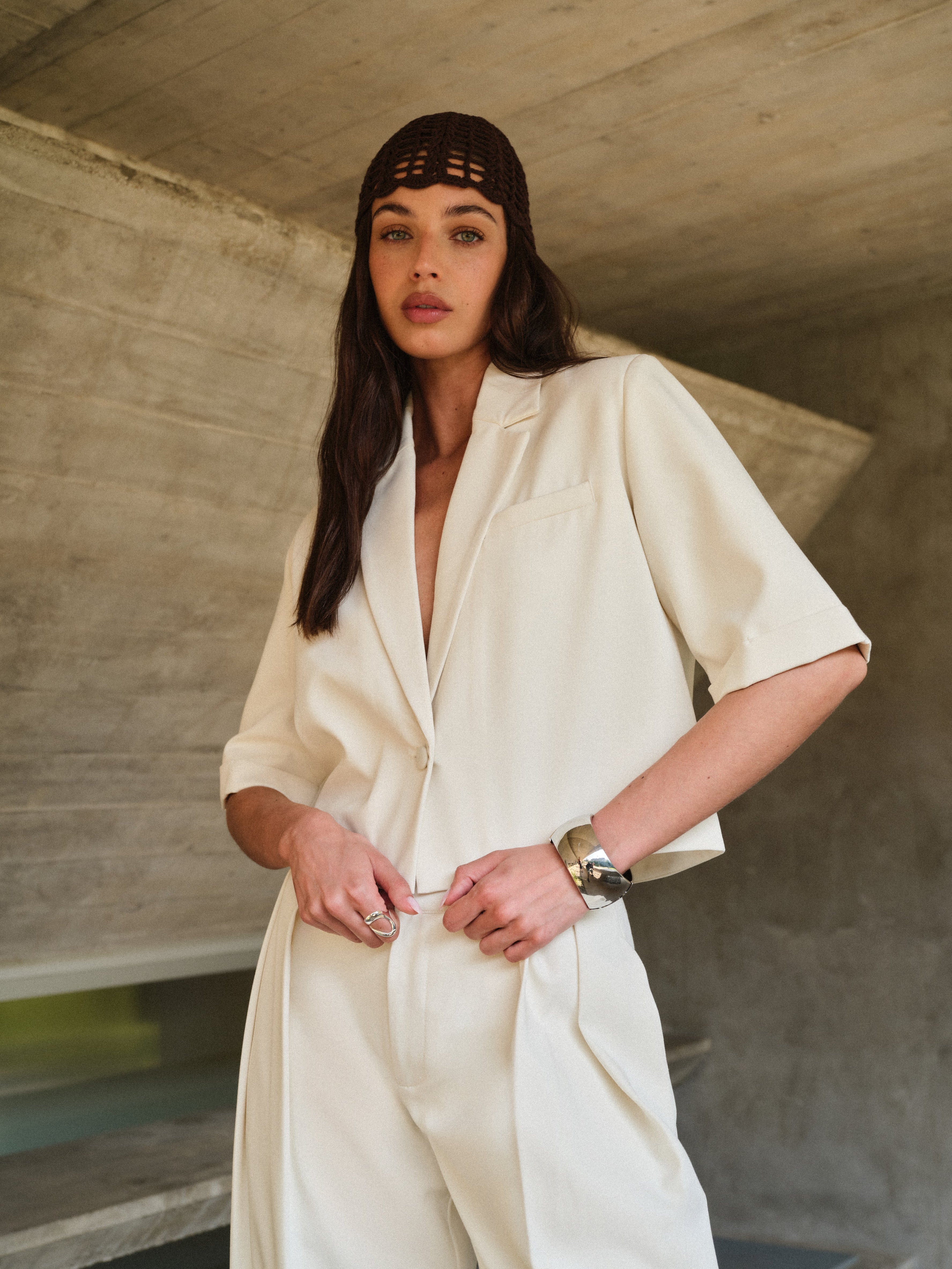 Woman wearing a white tailored blazer with brown a textured headband in an indoor setting