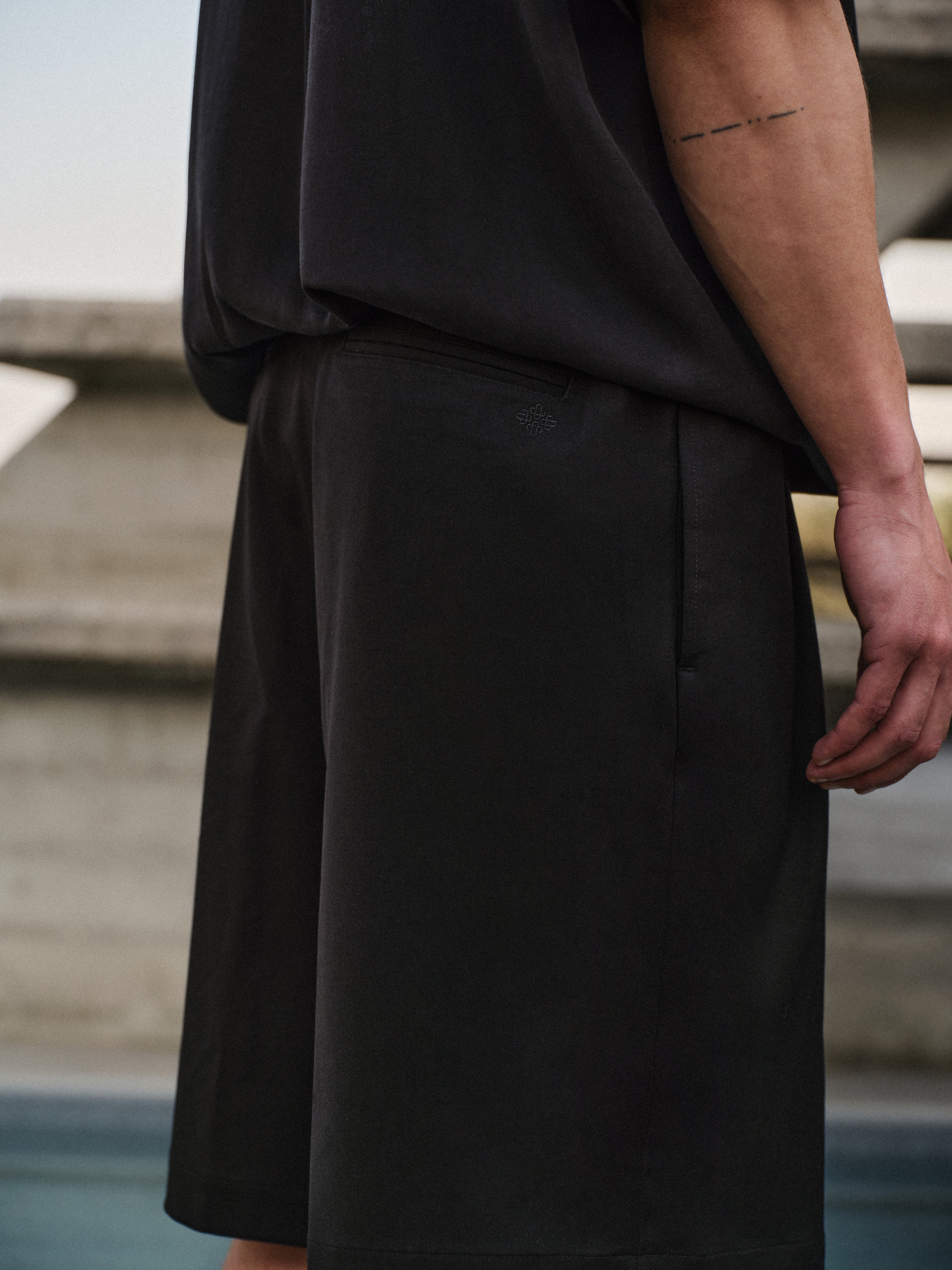Close up of a man wearing black tailored shorts standing on a concrete floor with a blurred background
