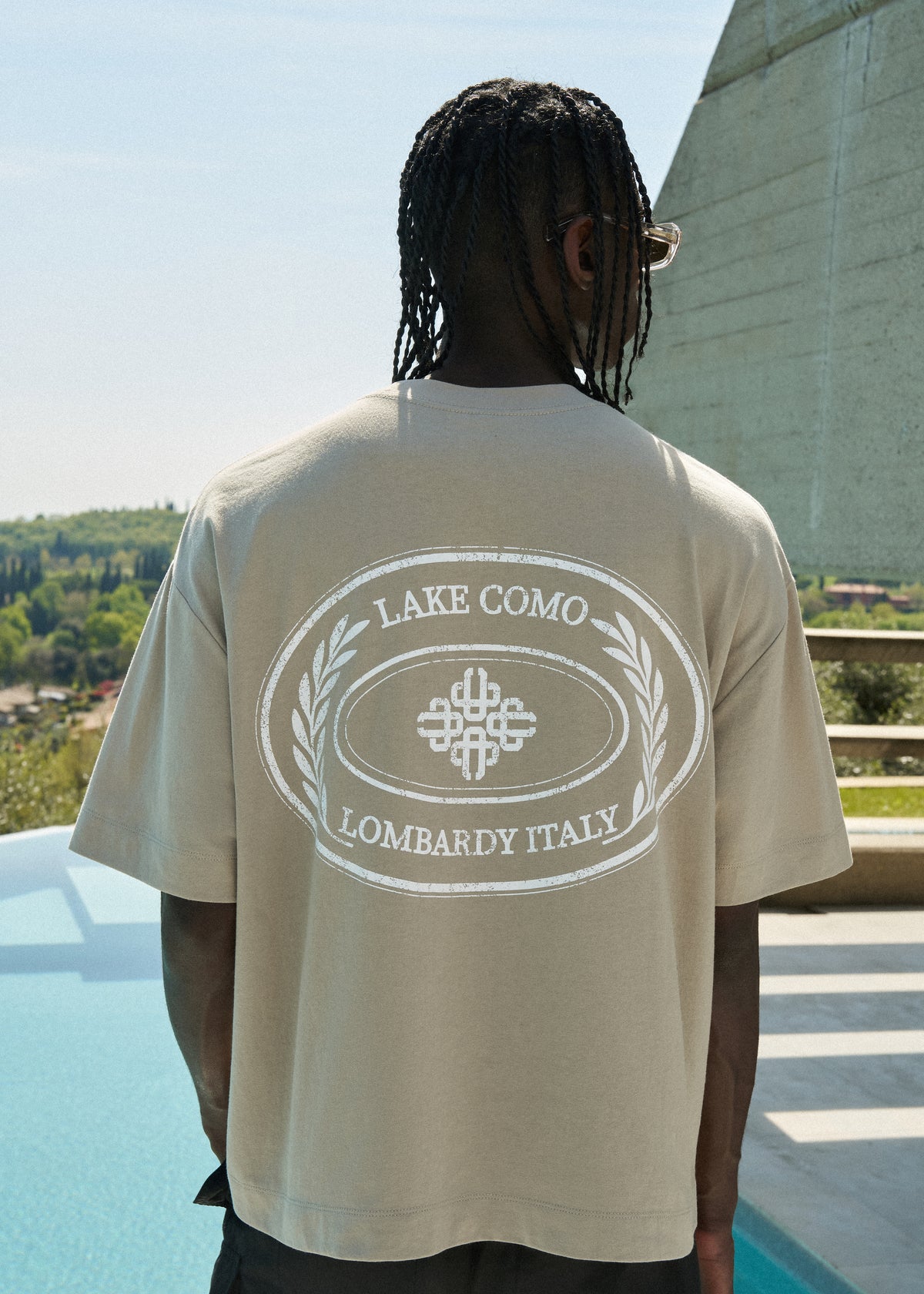 Man wearing a beige t-shirt with 'Lake Como Lombardy Italy' print outdoors.