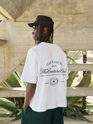 Person wearing a white t-shirt with text and graphics, standing outdoors.