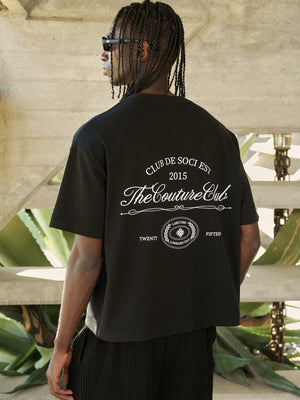 Person wearing a black t-shirt with branding text and logo outdoors.