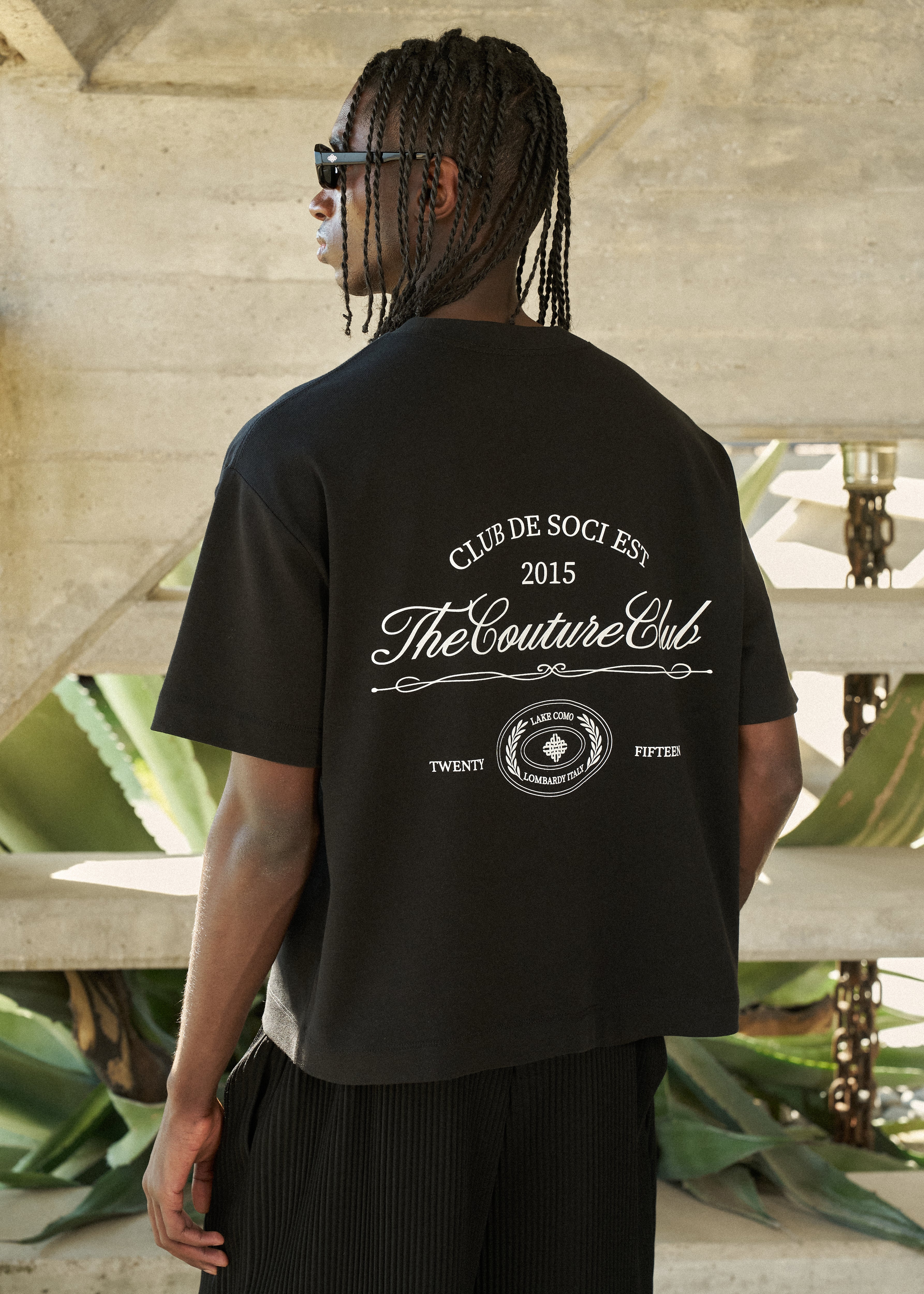 Person wearing a black t-shirt with branding text and logo outdoors.