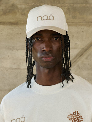 Man wearing a beige cap and white shirt with branding against a neutral background
