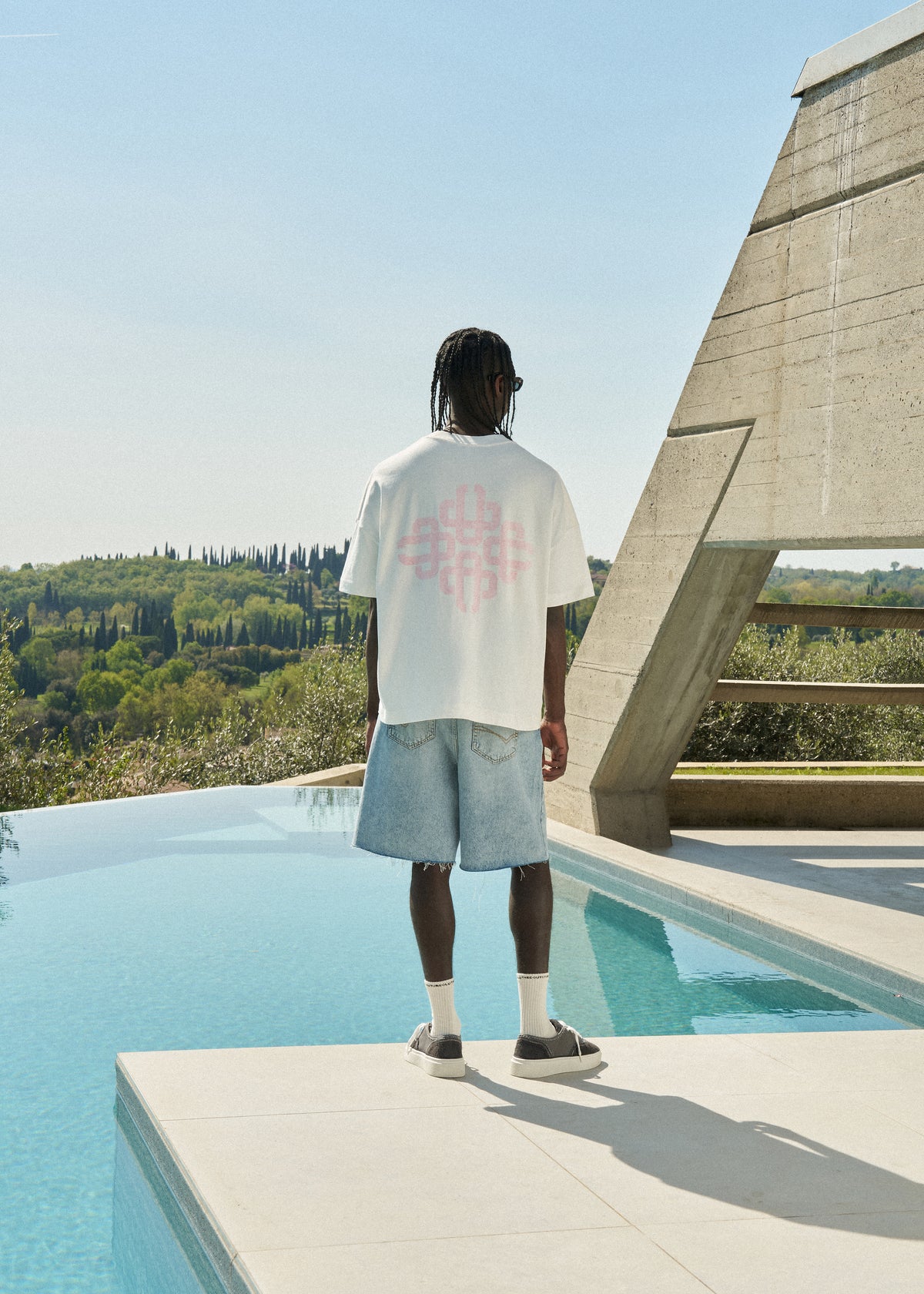 Person wearing a white t-shirt with pink graphic on the back and light blue denim shorts.