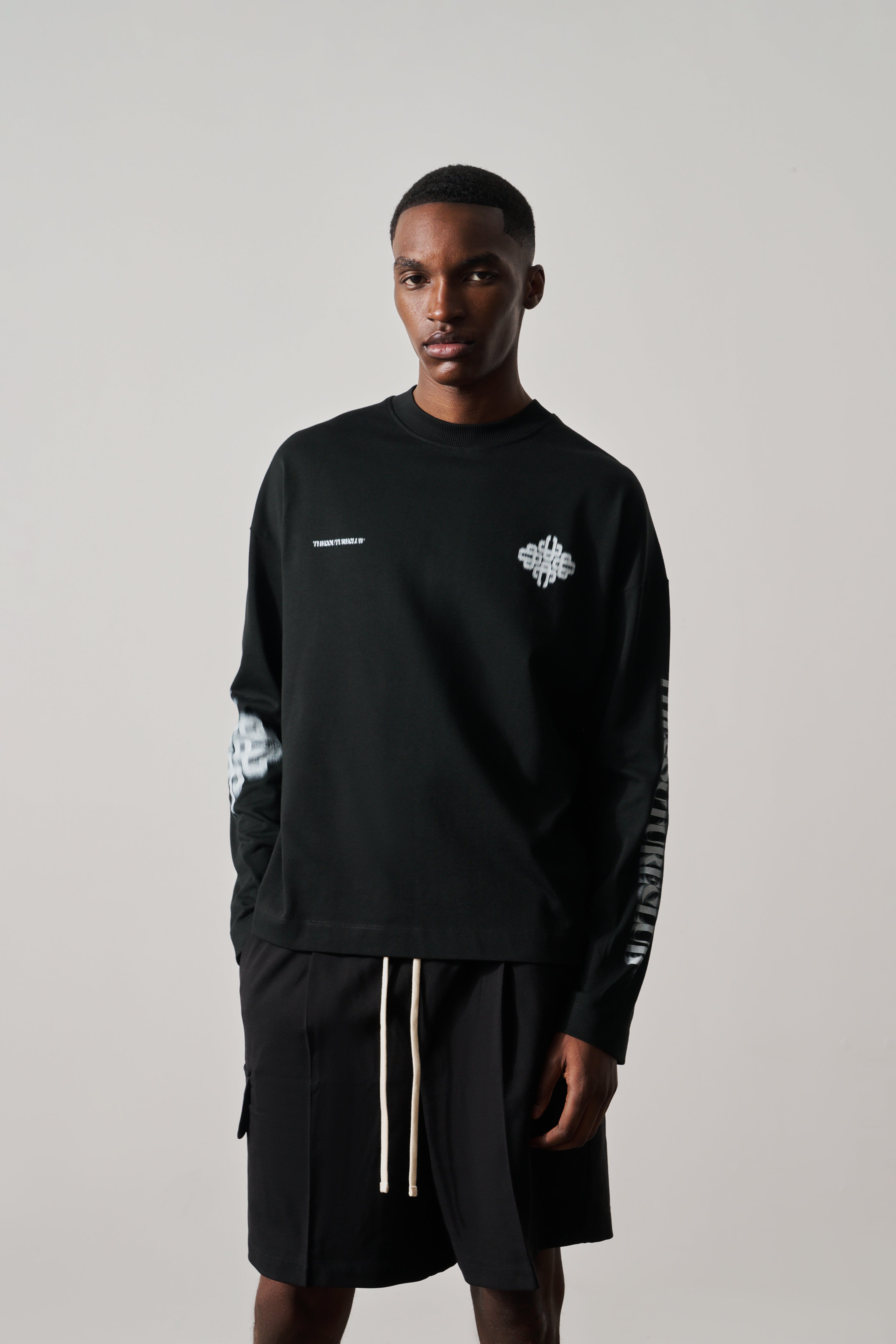 Man wearing a black long-sleeved t-shirt with white graphics on a plain background