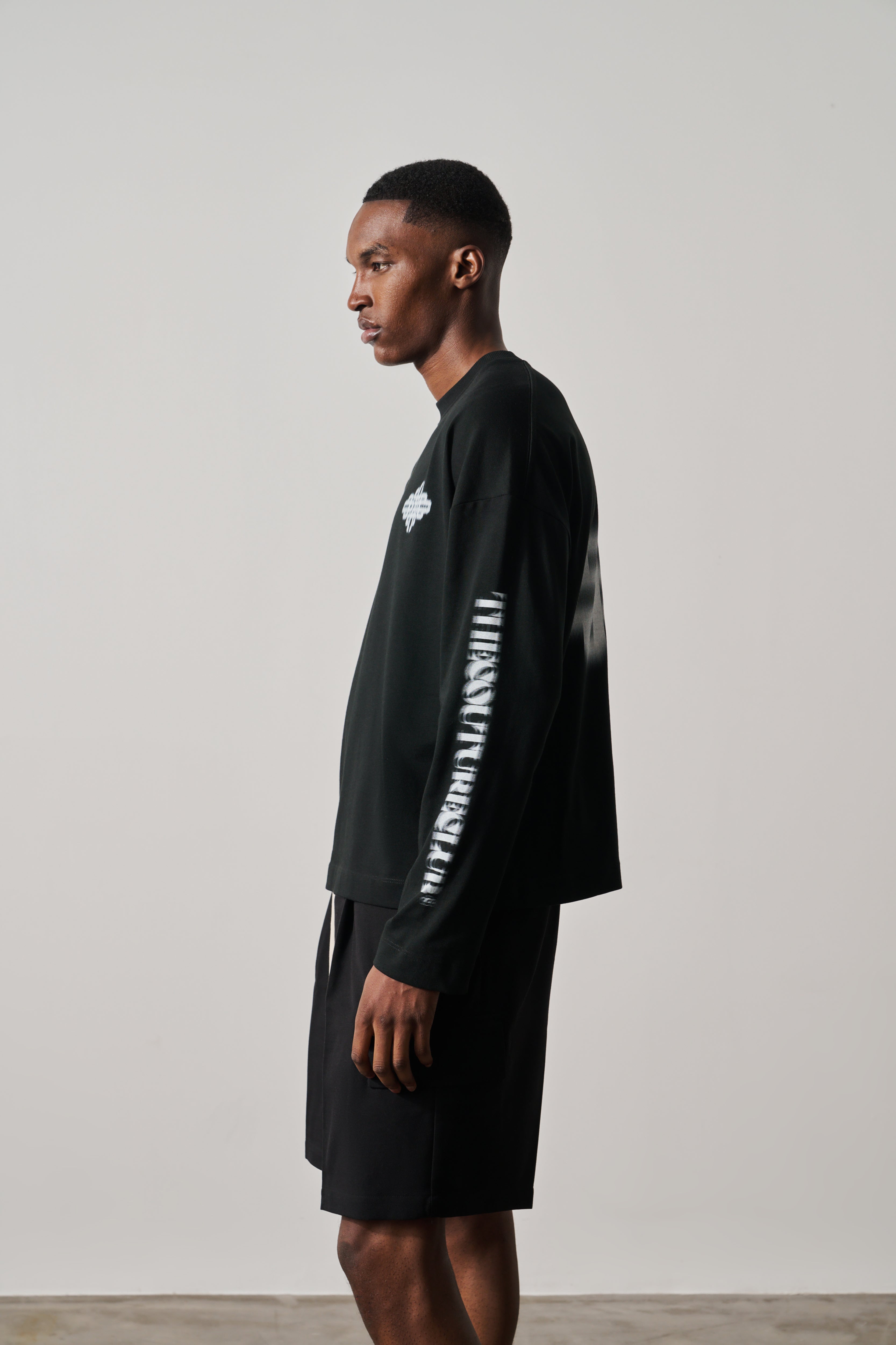 Man wearing a black long-sleeve t-shirt with white text on sleeves against a plain background