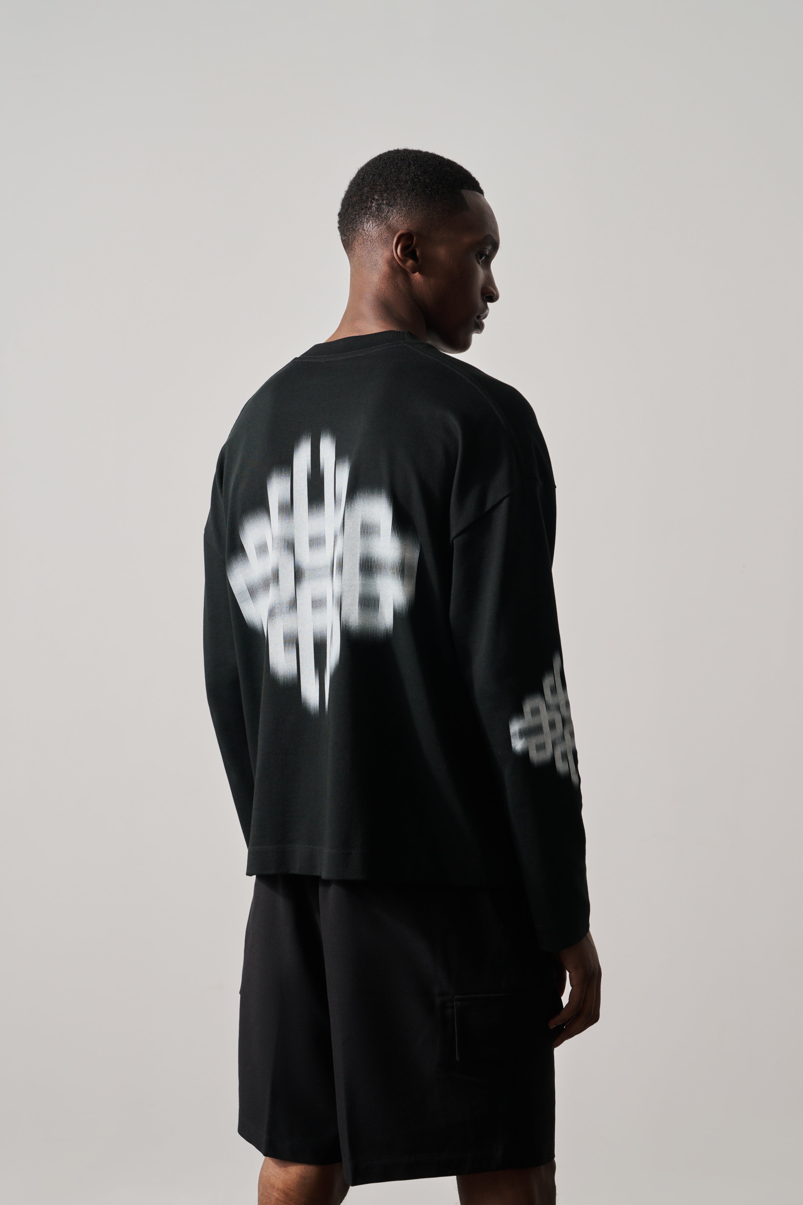 Person wearing a black outfit with white branded artwork on a plain background