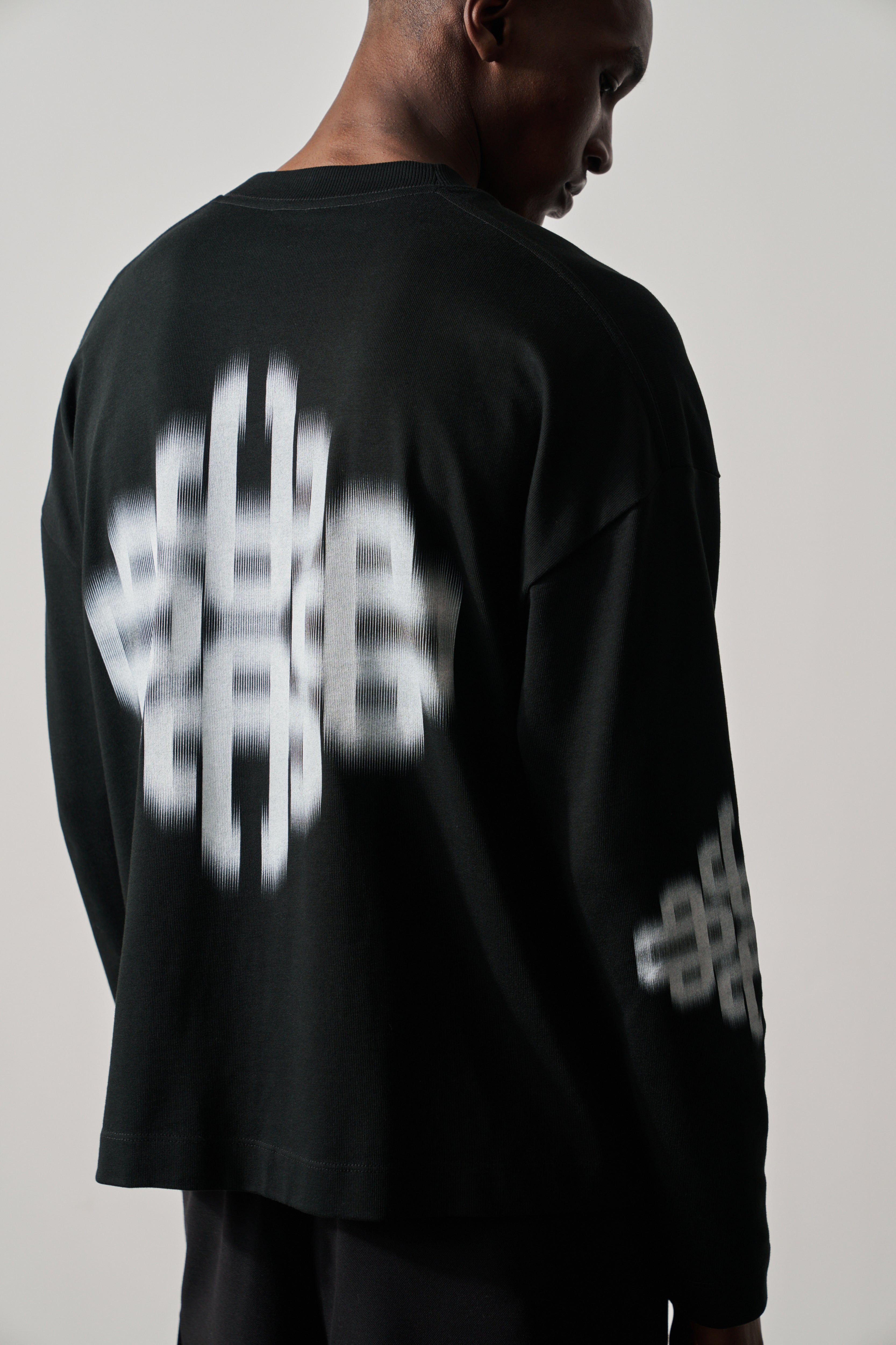 Person wearing a black long-sleeve t-shirt with white geometric designs on a plain background