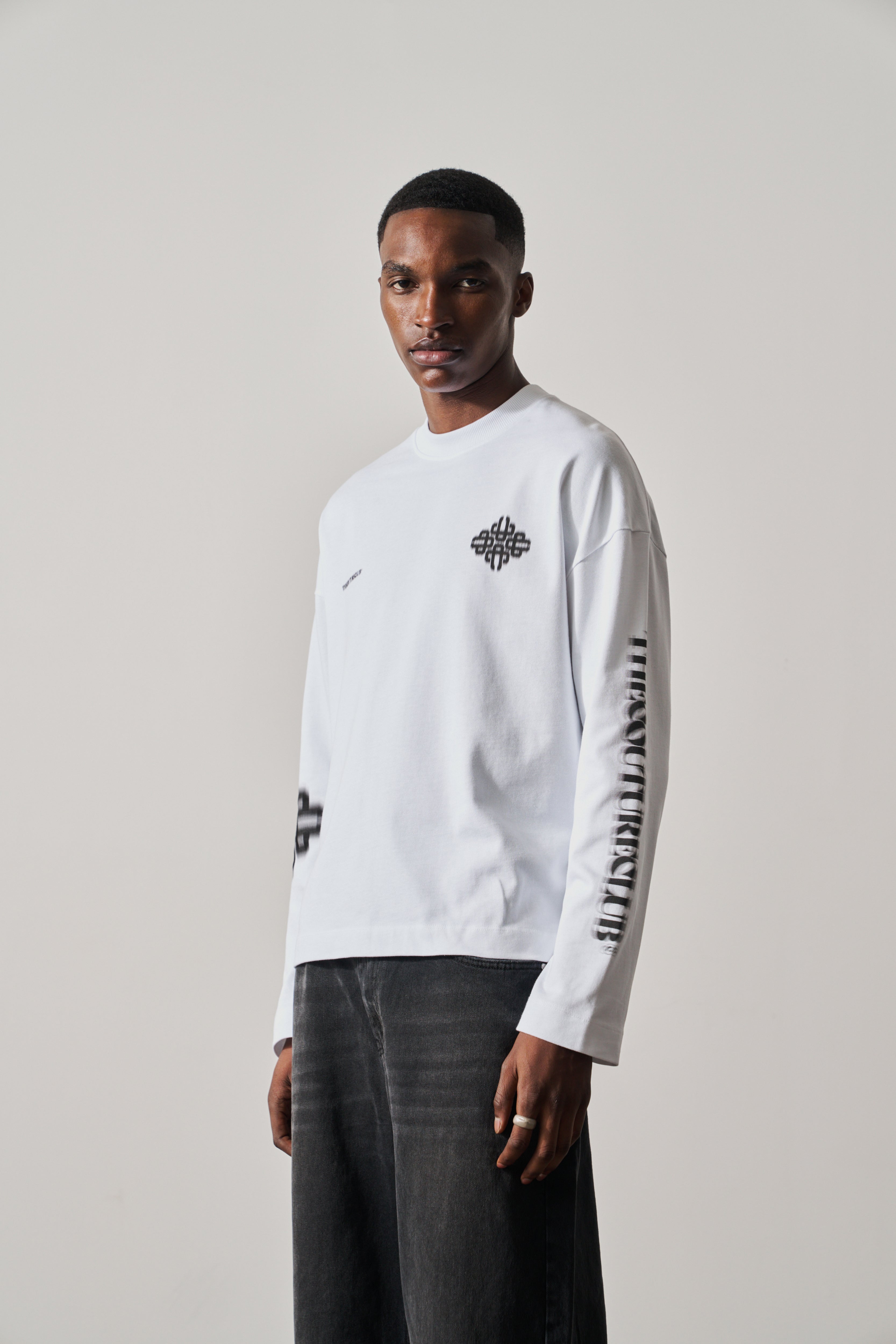 Man wearing a white long-sleeve t-shirt with black graphics on a plain background