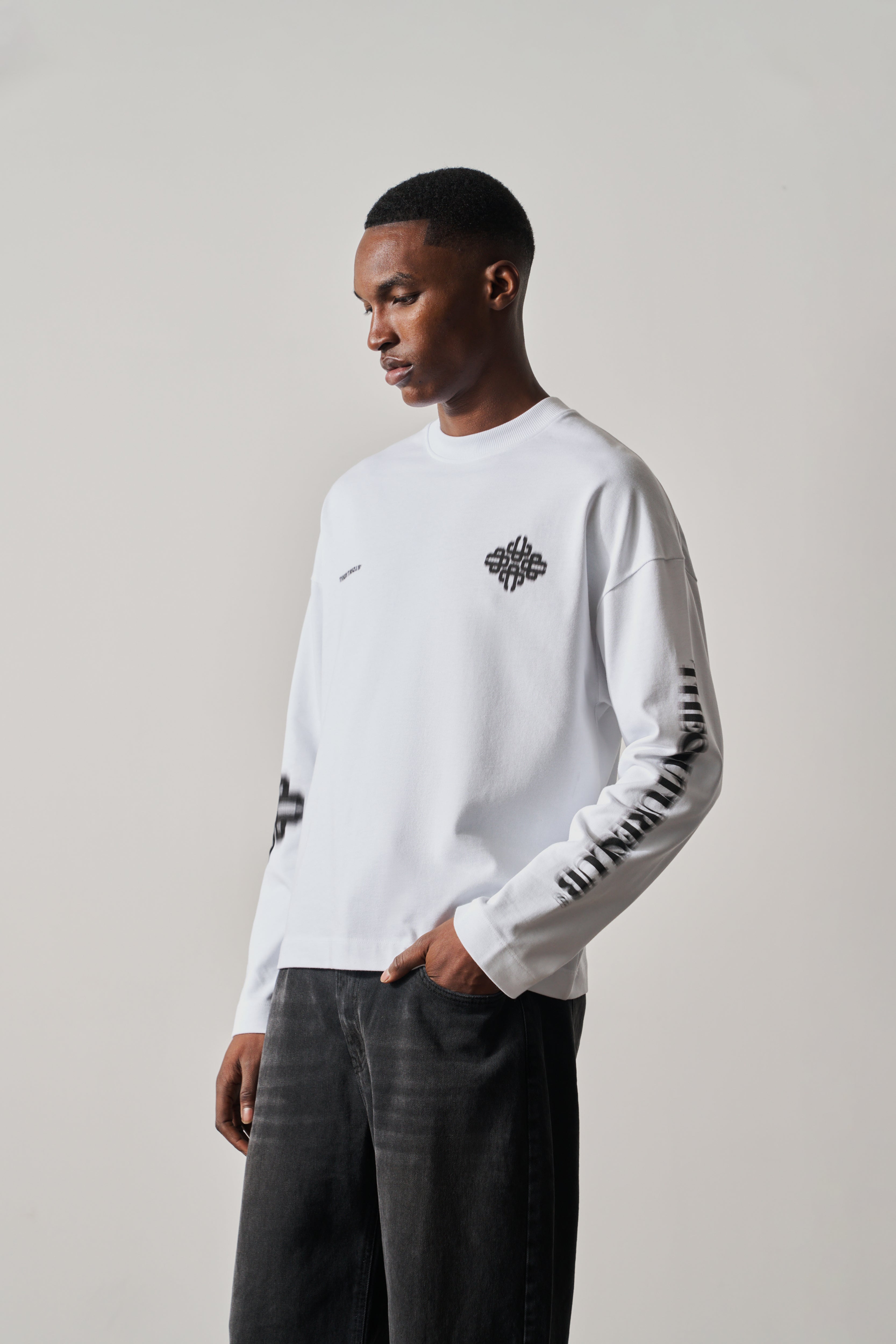 Man wearing a white long-sleeve t-shirt with black designs on a plain background