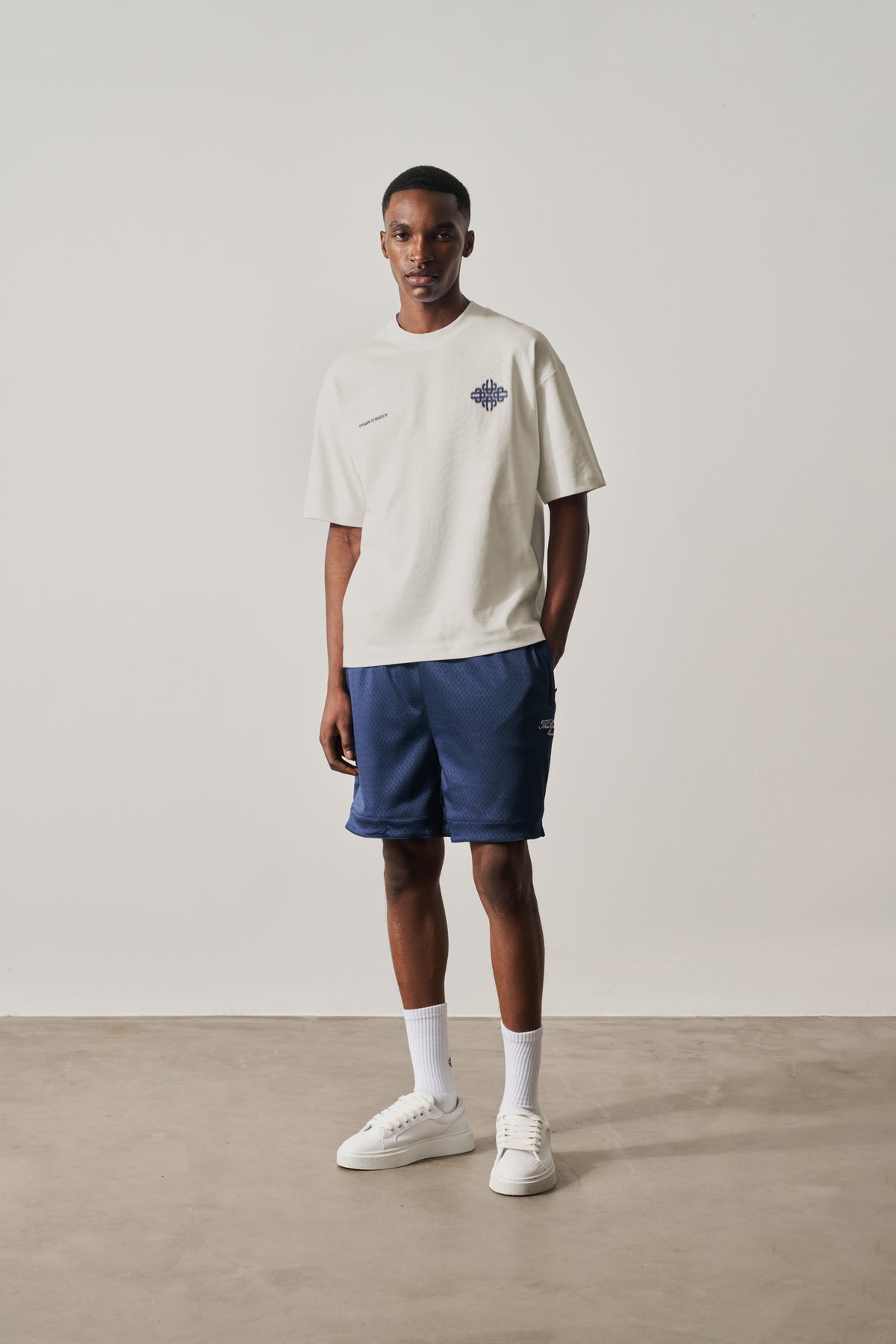 Man wearing a white t-shirt with a logo and blue shorts on a plain background